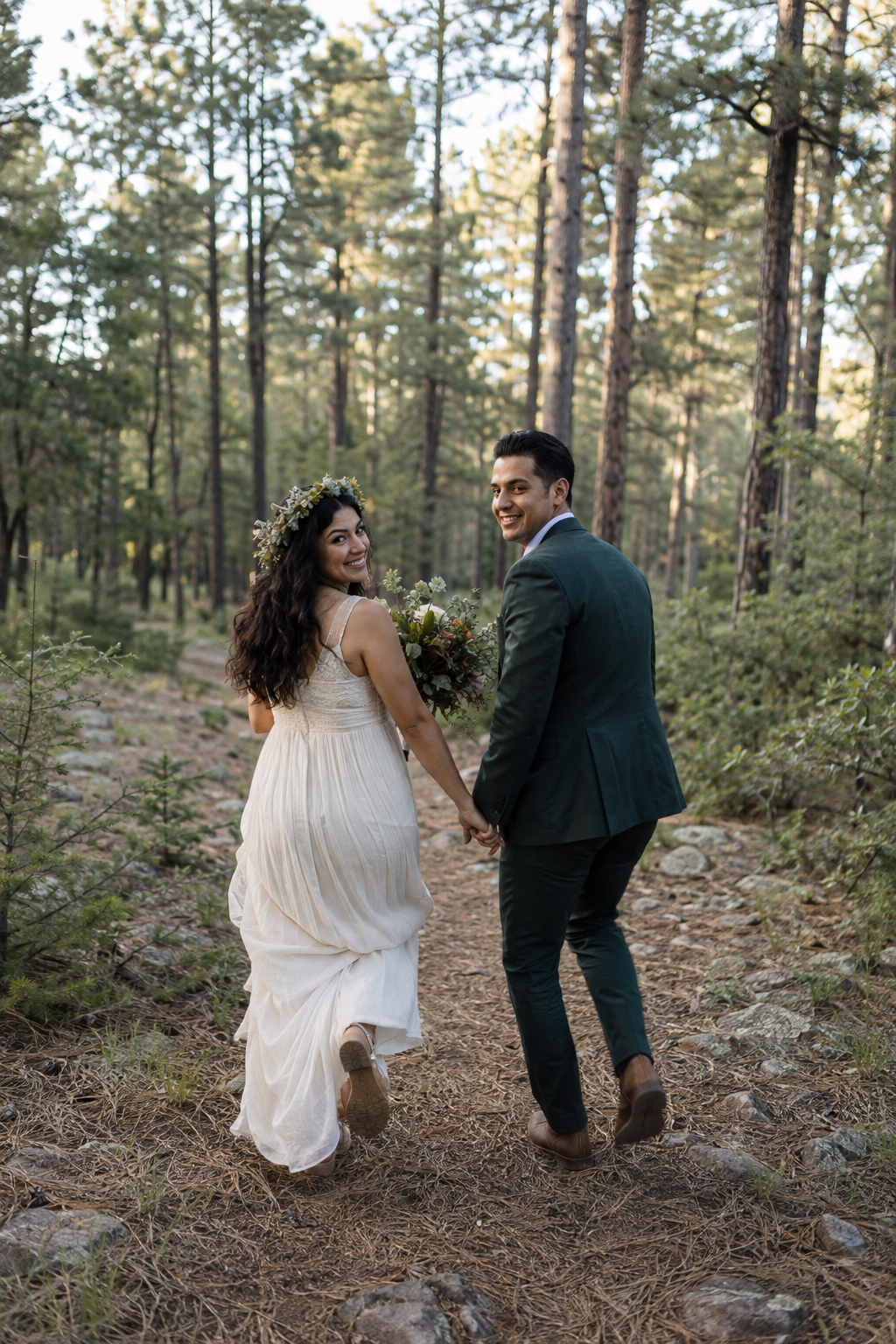 A happy couple holding hands and walking in a forest during daytime, wearing wedding attire, with the woman holding a bouquet and wearing a floral headband.