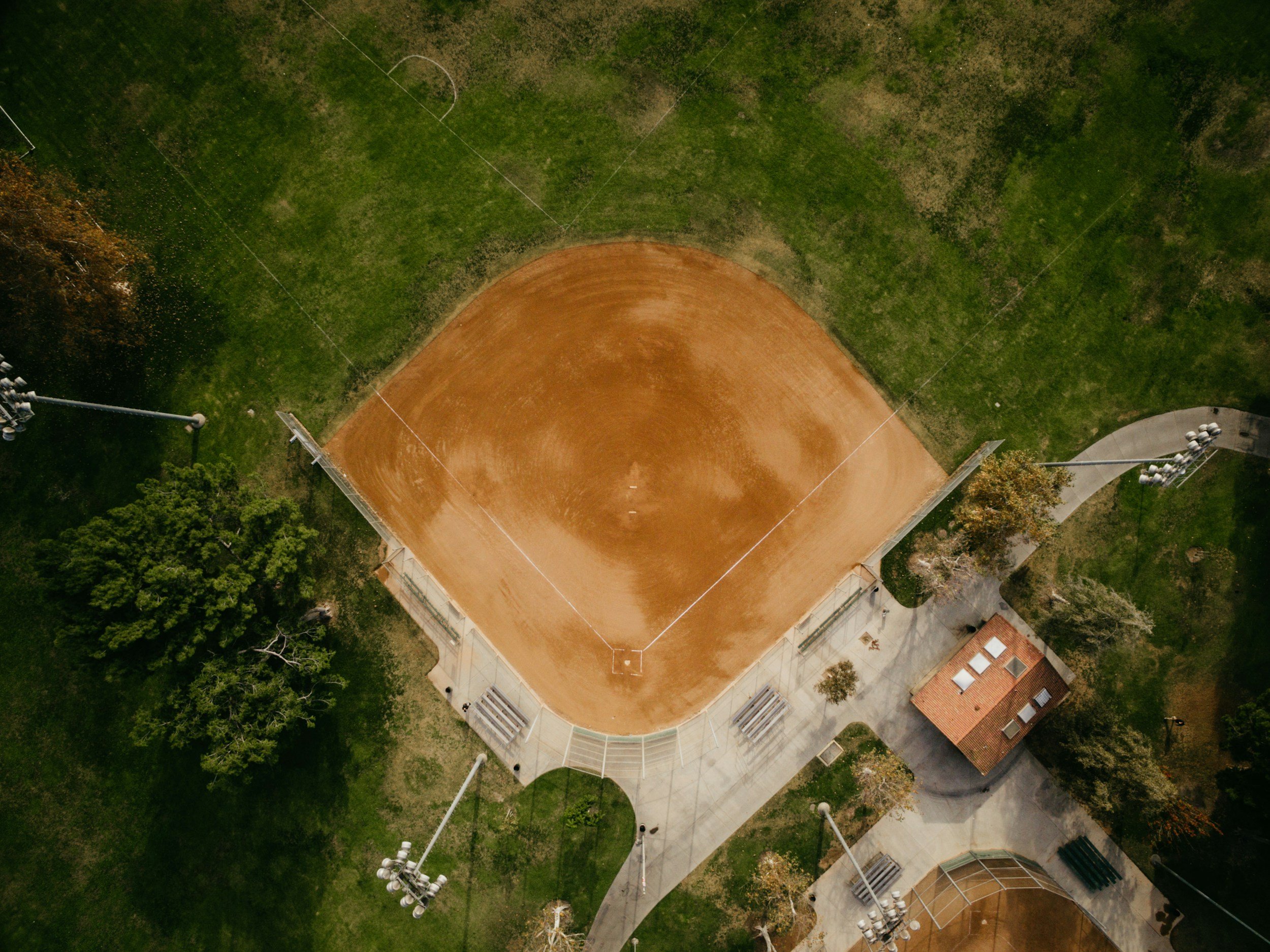 An aerial view of a baseball field with surrounding green grass, trees, and walking paths.