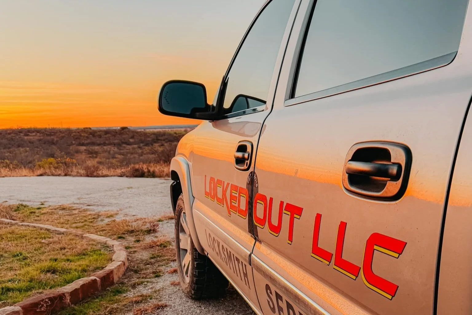 Side view of a locksmith service vehicle with "Locked Out LLC" text, parked on a scenic landscape during sunset.