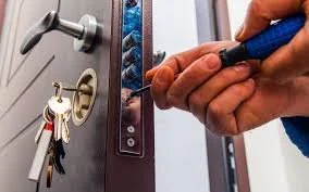 Person using screwdriver to install or repair a door lock, with keys hanging from the lock.