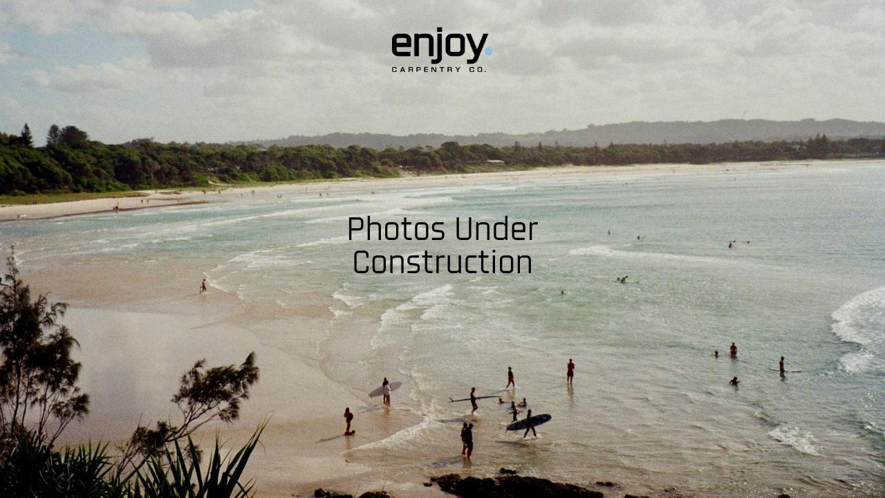 Beach with people surfing and swimming, green trees and hills in the background, cloudy sky