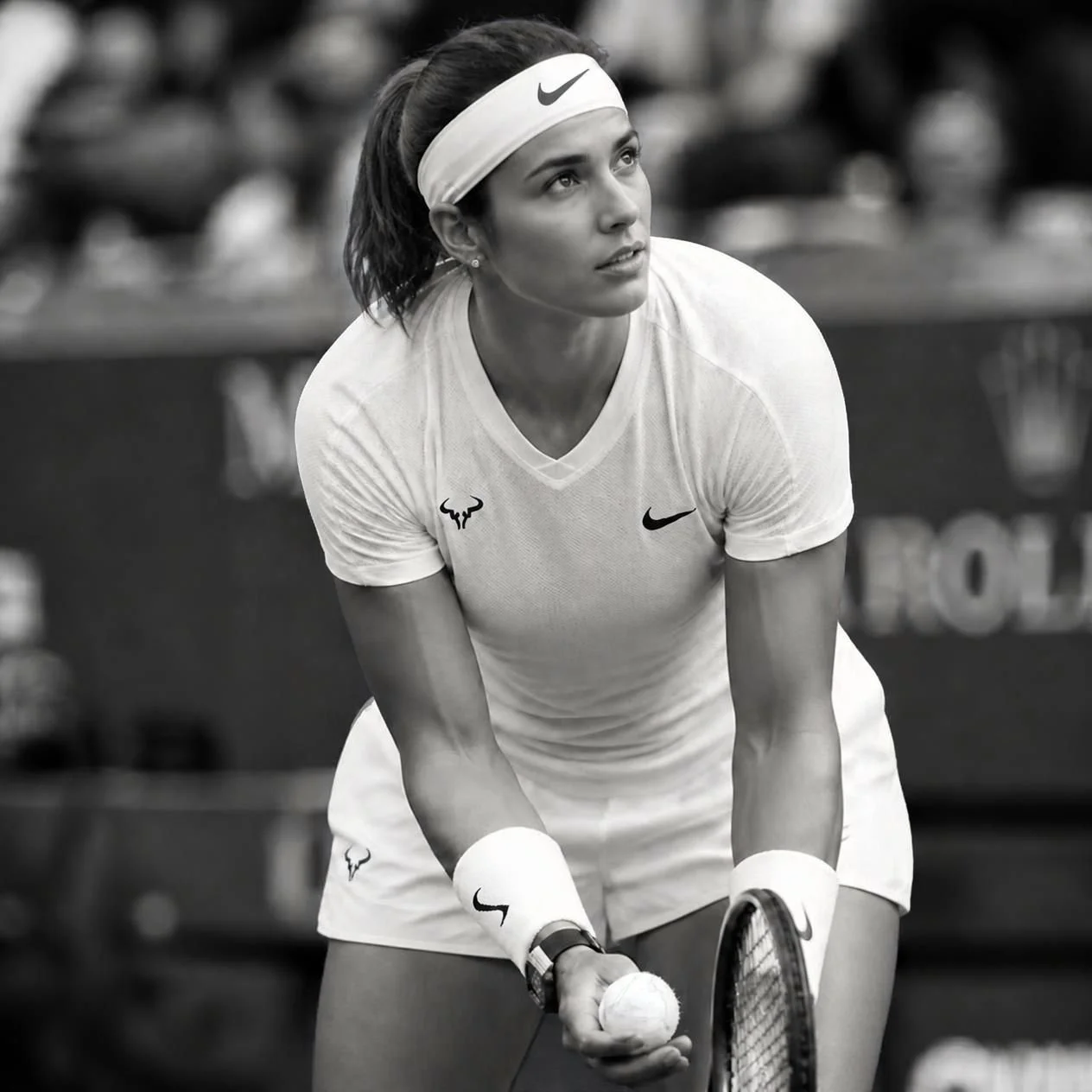 A female tennis player in a white Nike shirt and headband, preparing to hit a tennis ball during a match.