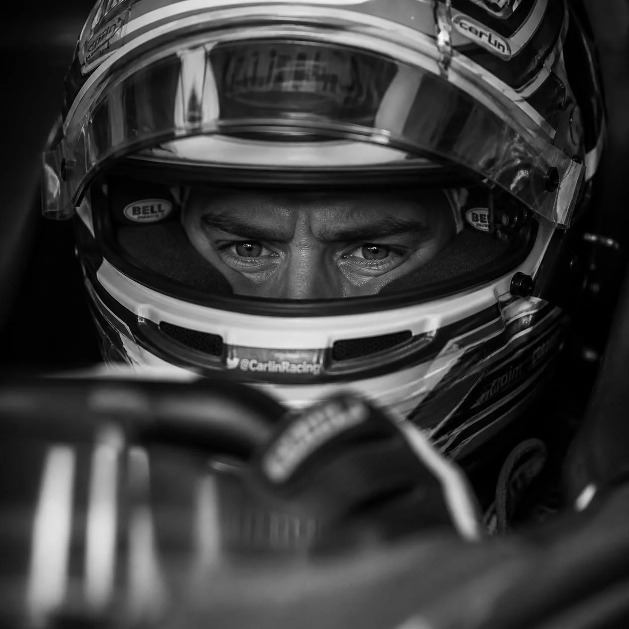Close-up of a race car driver wearing a helmet, looking intensely forward, with focus on their eyes in black and white.