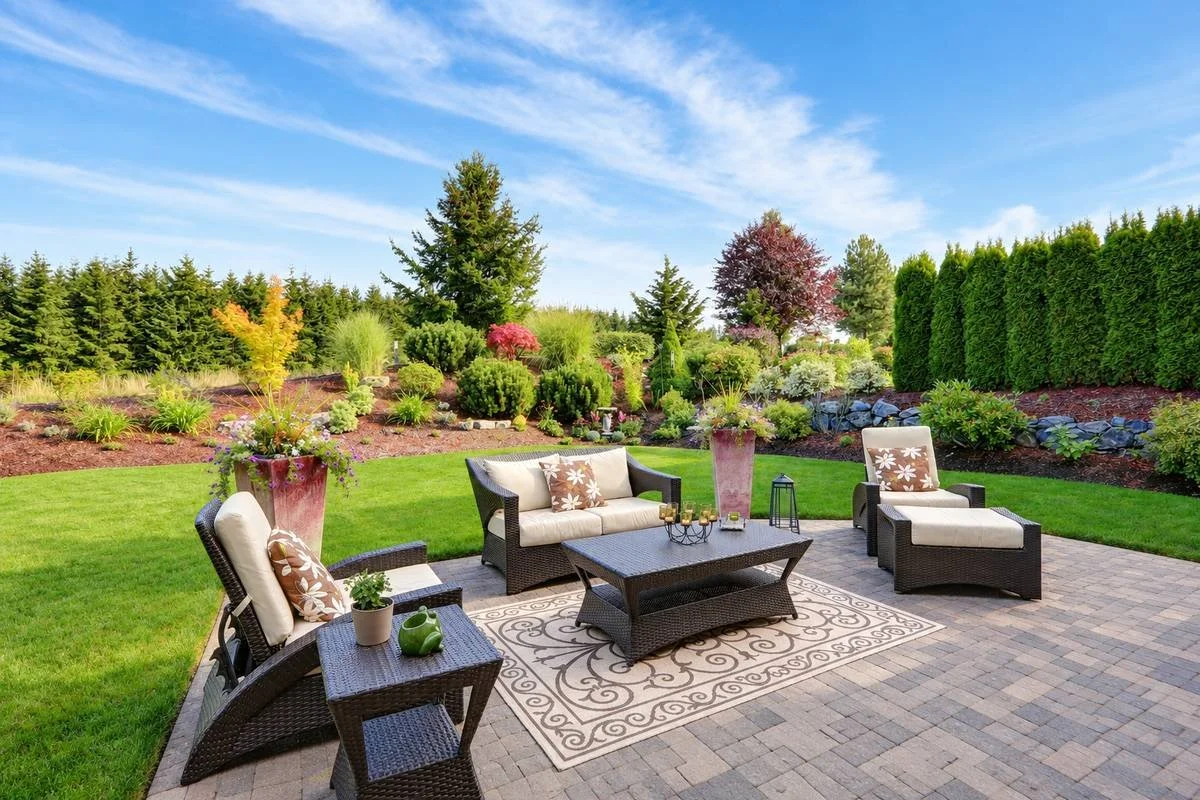 Paver patio seating area surrounded by a green lawn and layered planting beds