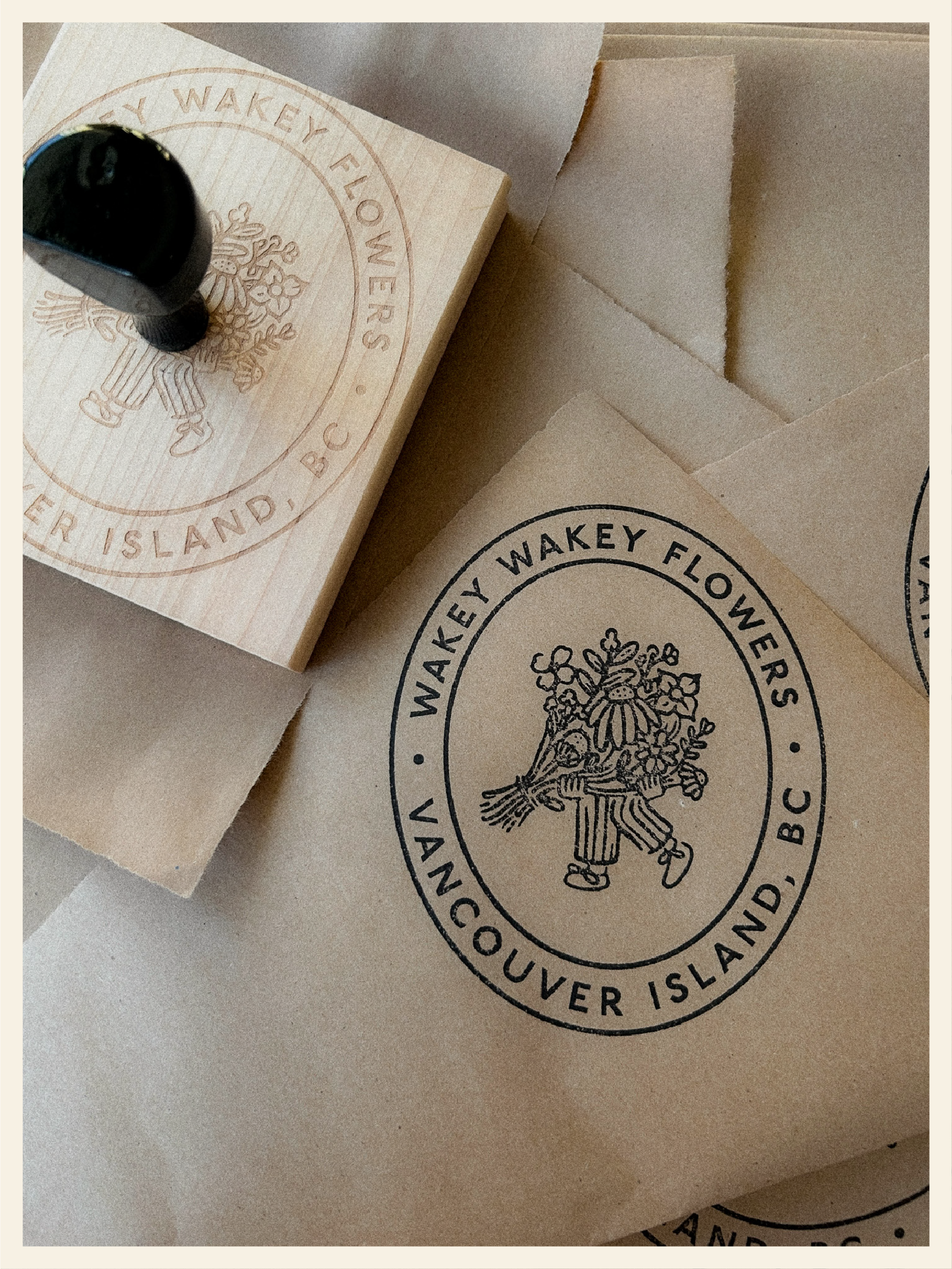 A wooden block with a circular logo that reads 'Wakey Flowyers' and 'Vancouver Island BC,' featuring a bee with flowers. Next to the block are stacked boxes with the same logo and design.