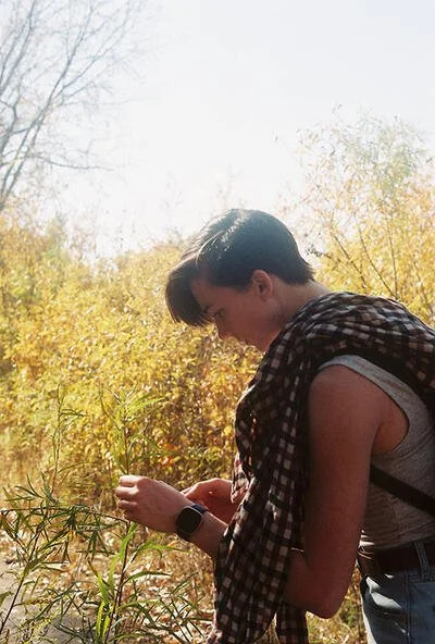Elyssa (a white person with short brown hair) leans down to examine a leaf