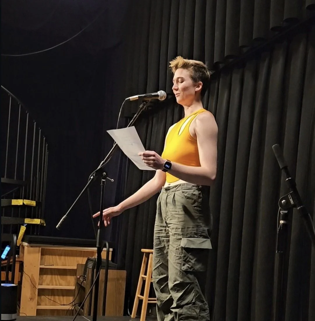 Elyssa wearing a yellow shirt standing at a microphone