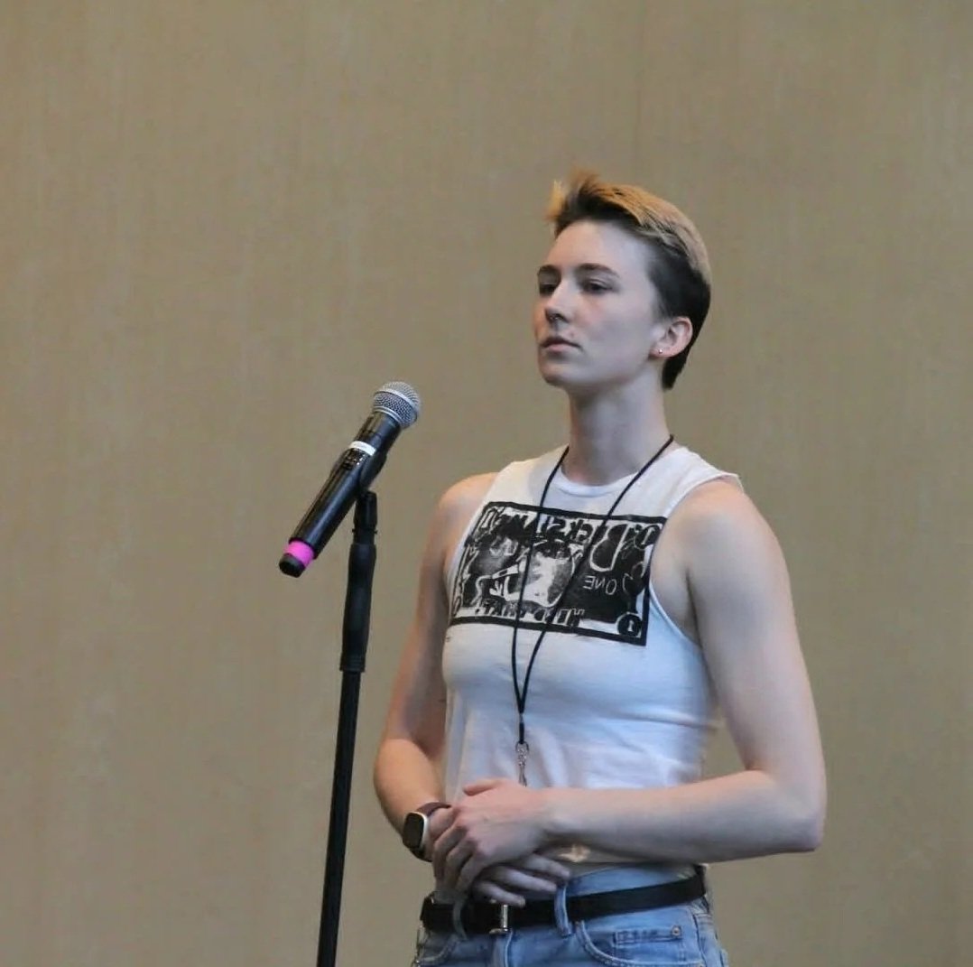 Elyssa in a white shirt standing at a microphone