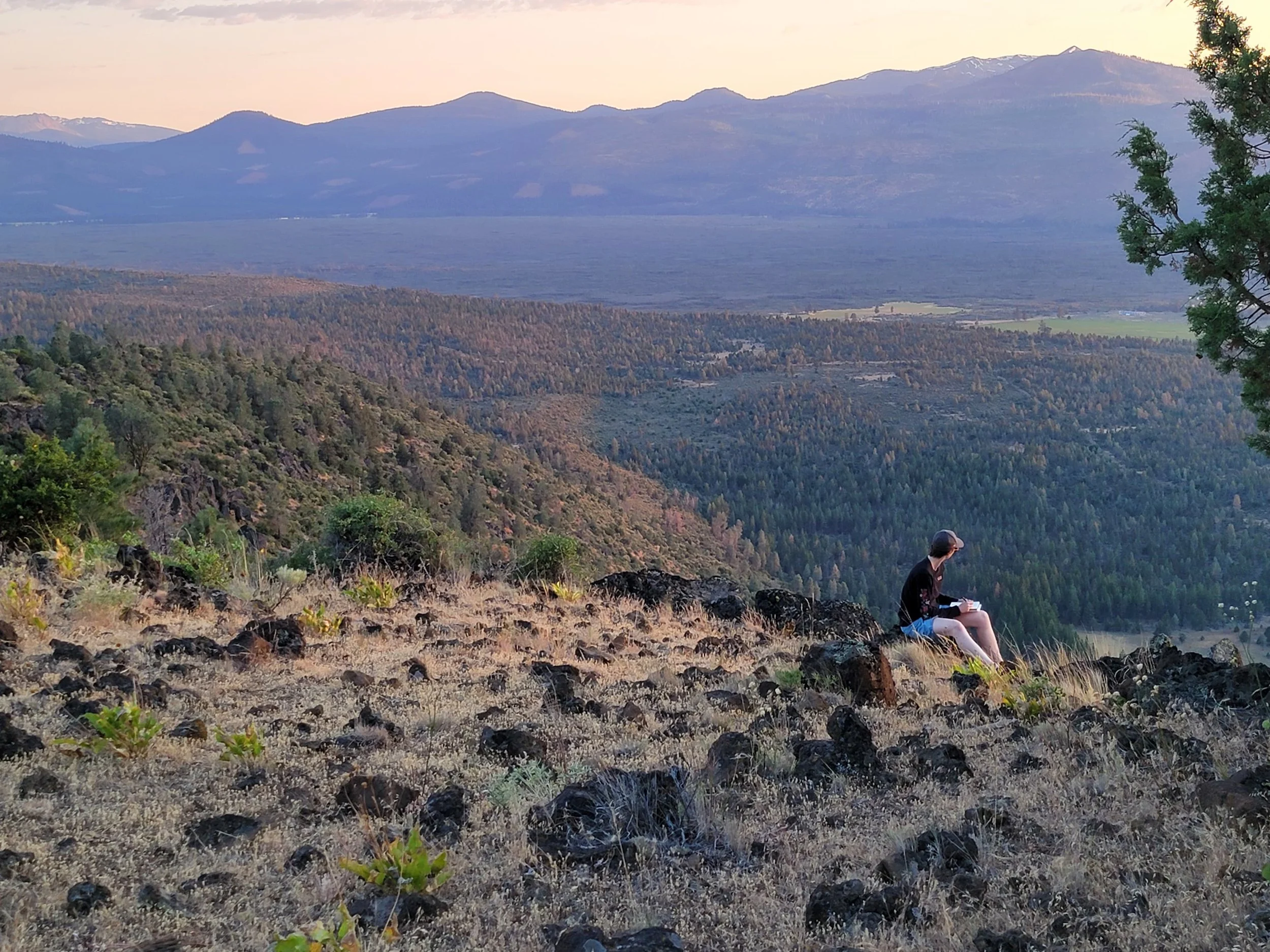 Zoomed-out photo of Elyssa sitting on a rock overlooking a valley
