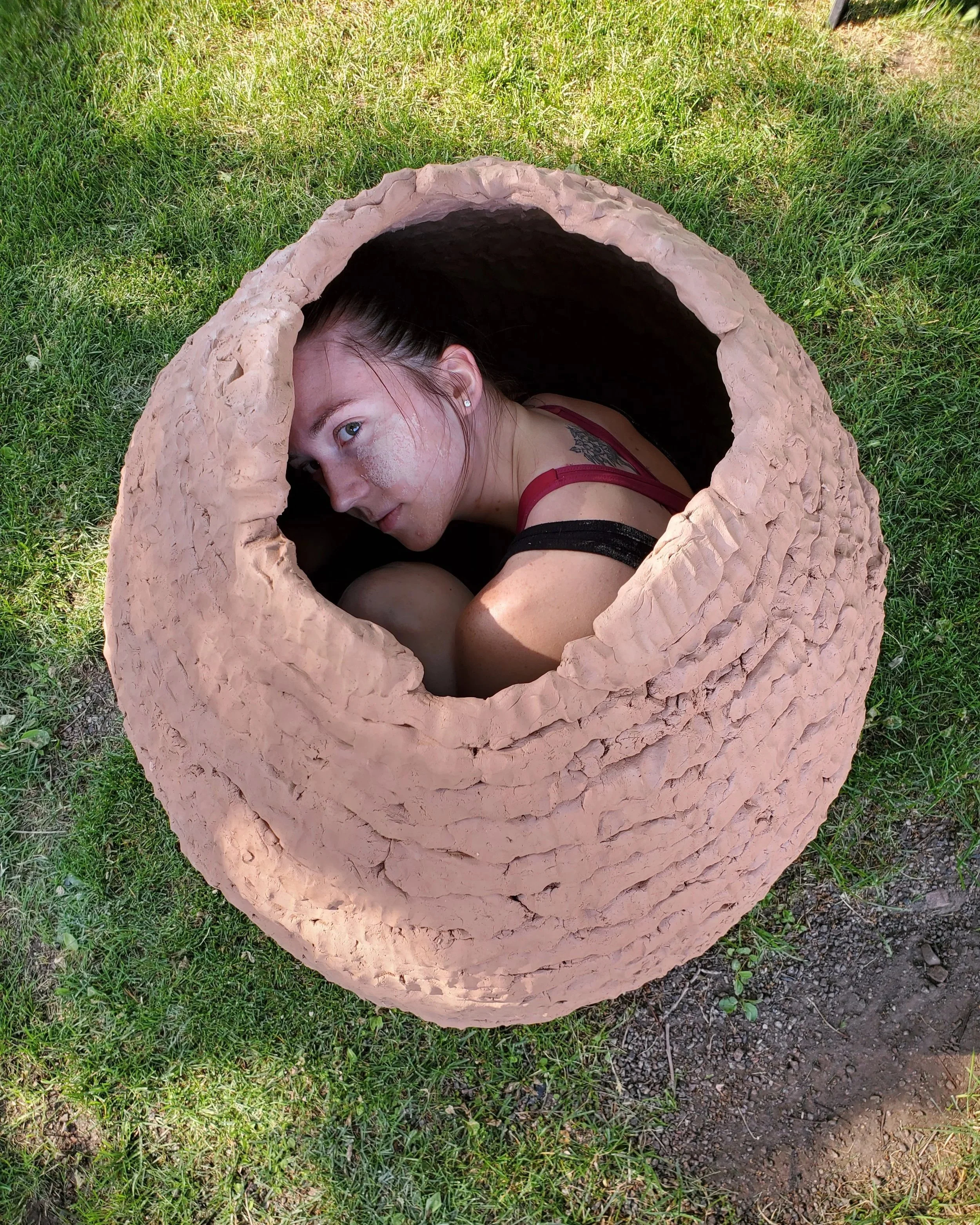 Elyssa peering out of a clay cocoon