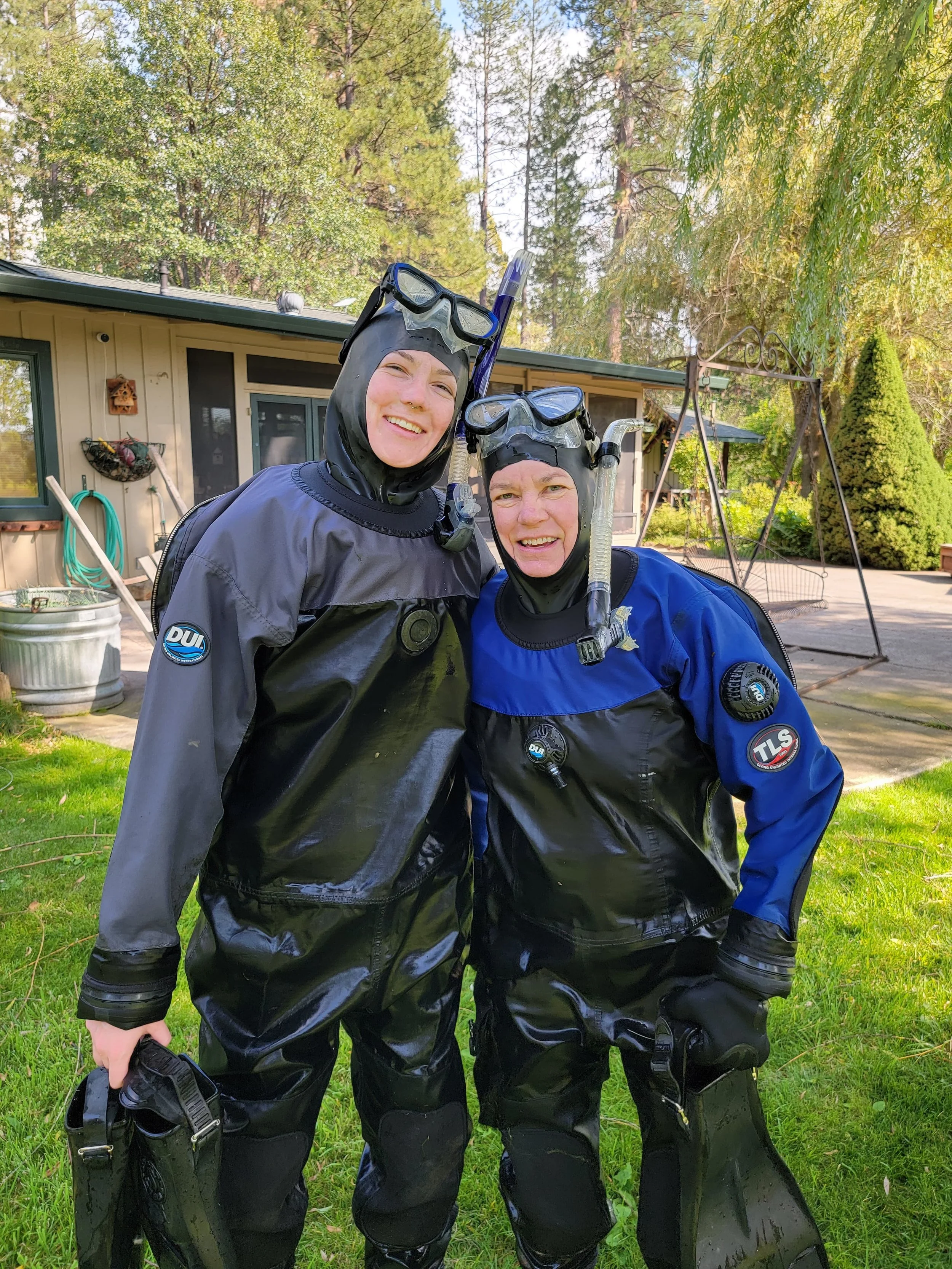 Two people standing on a lawn wearing wetsuits