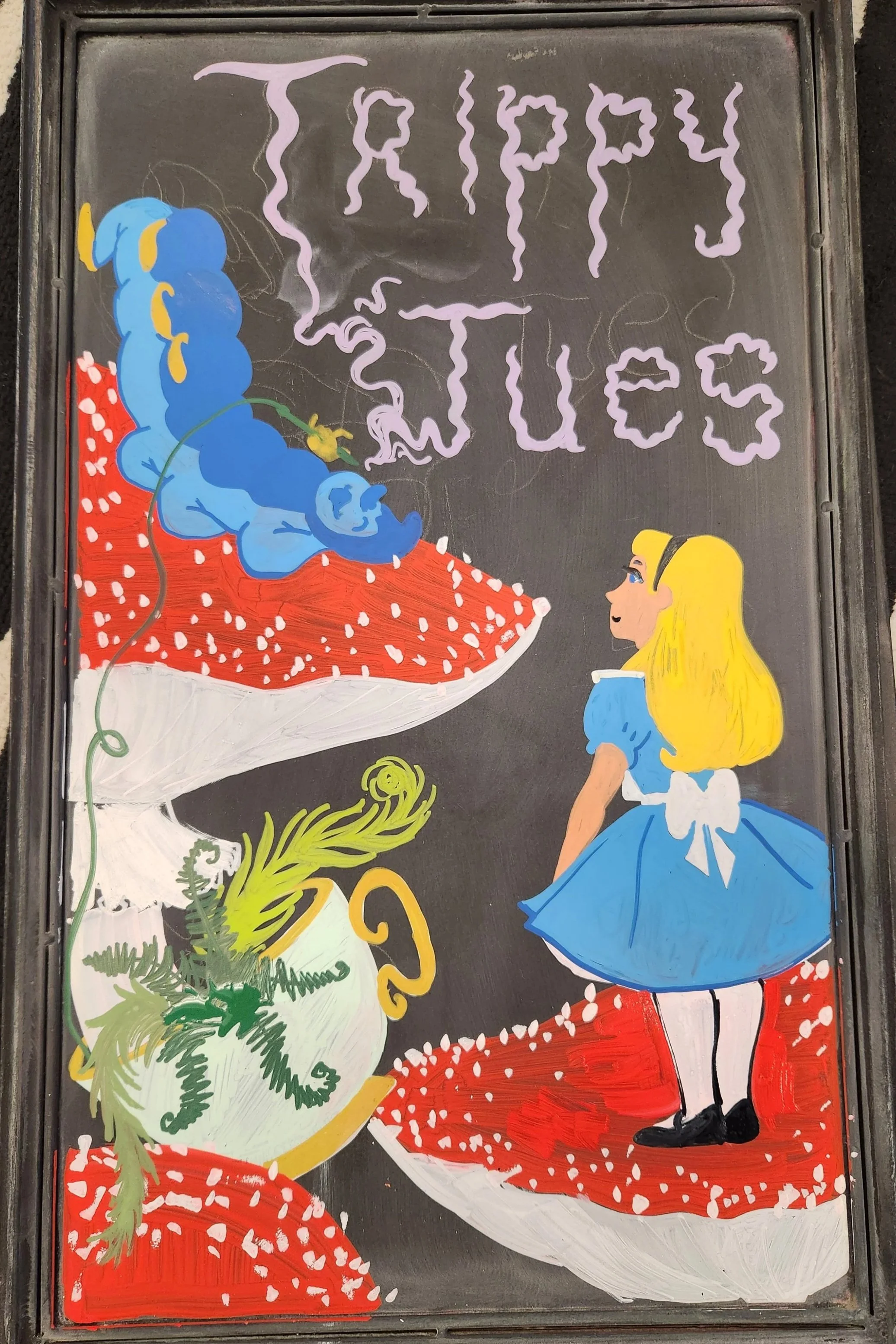Illustration of Alice from Alice in Wonderland, wearing a blue dress, sitting at a table with a large mushroom and a teapot. The words 'TRIP TOPICS' are written above in stylized purple letters.