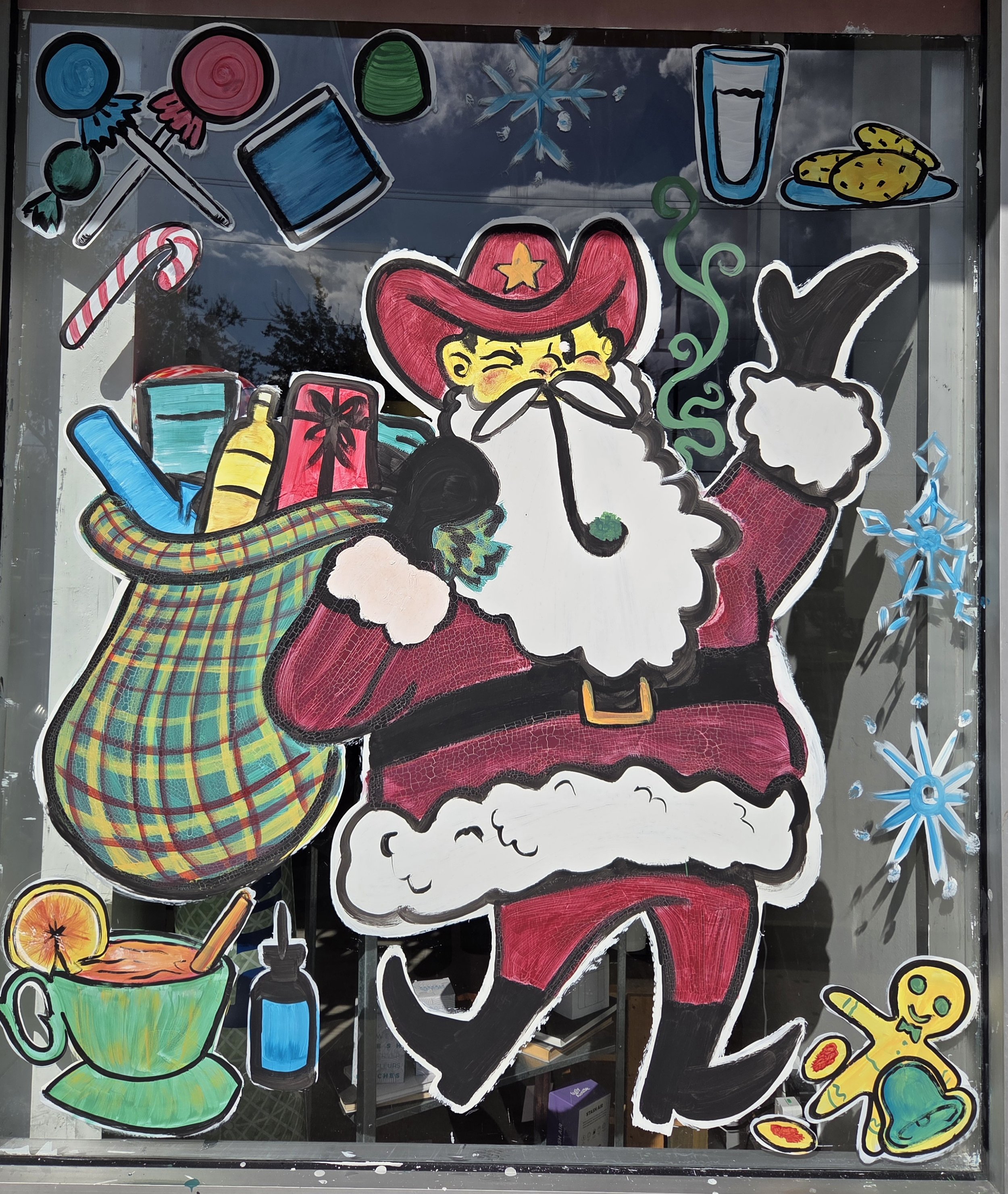 Colorful drawings of holiday-themed objects on a window, including a red cowboy hat with a star, a green and yellow plaid scarf, a plate of cookies, a glass of milk, a candy cane, a wrapped gift, a cup of hot chocolate, a snowflake, a stocking, a sli