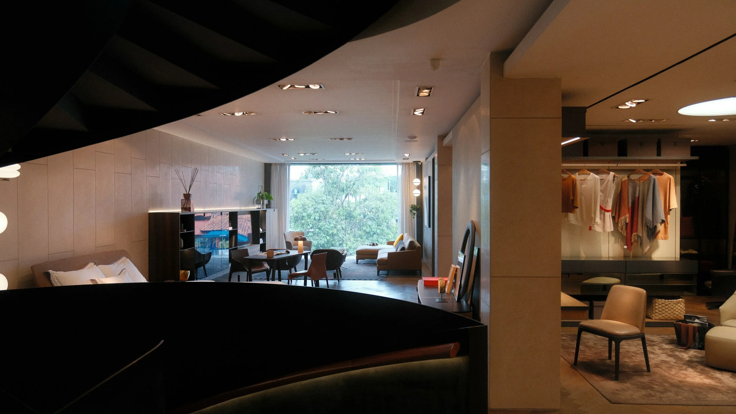 A modern hotel lobby with seating areas, a window with a view of trees, and clothing displayed on a rack.
