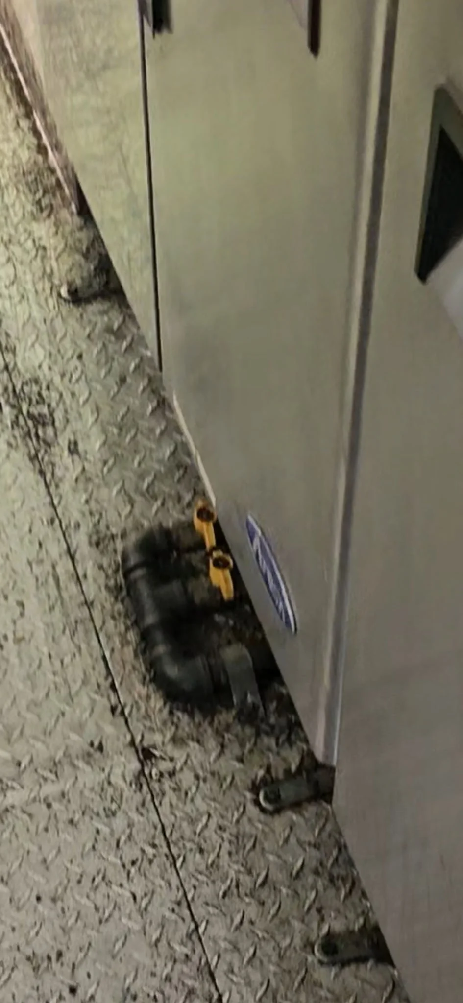 Close-up of a concrete floor with a pair of black shoes, a yellow spirit level, and a large metallic machine or equipment.