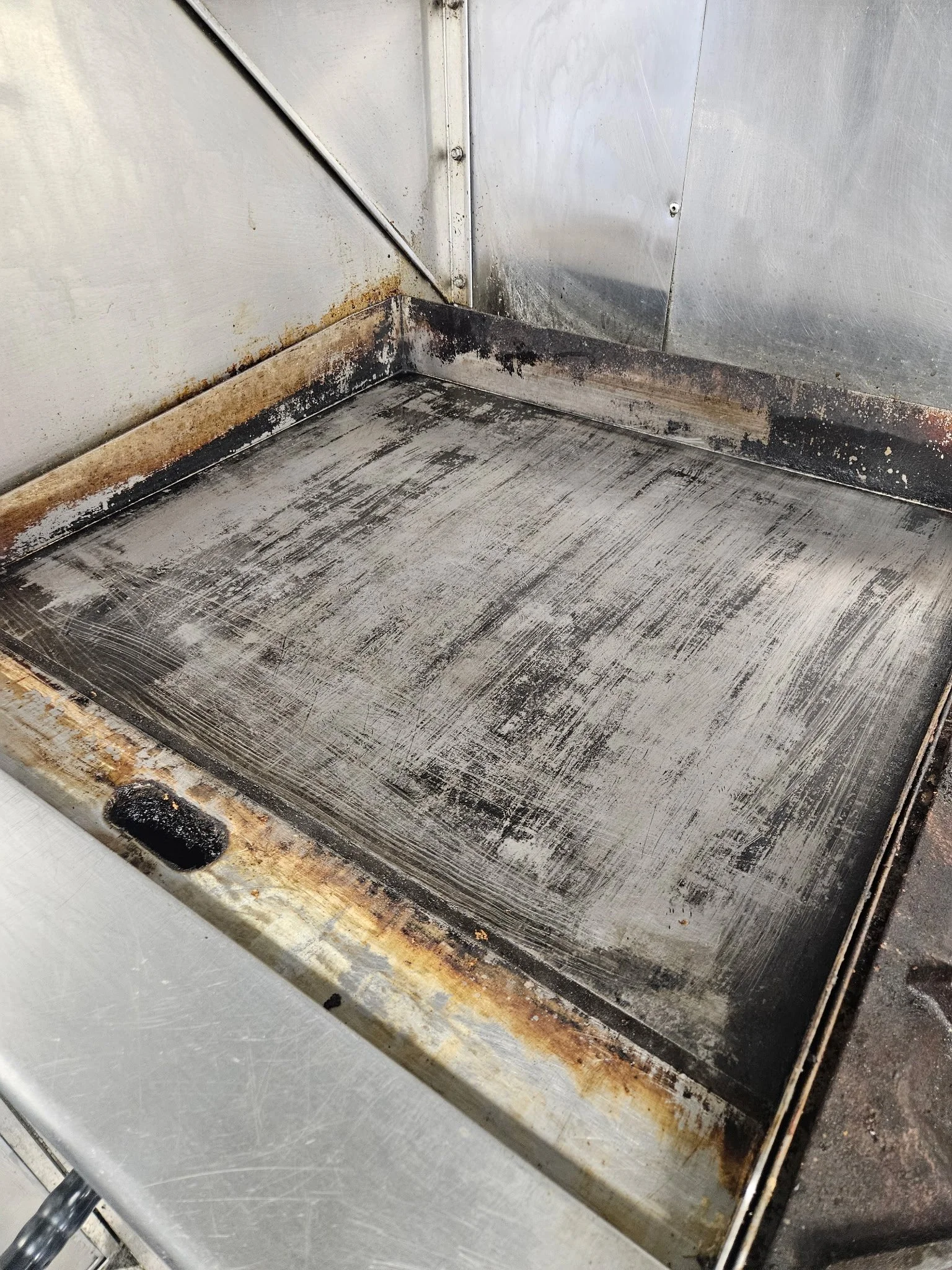 A stainless steel kitchen oven or stovetop with visible rust and stains on the surface and edges.