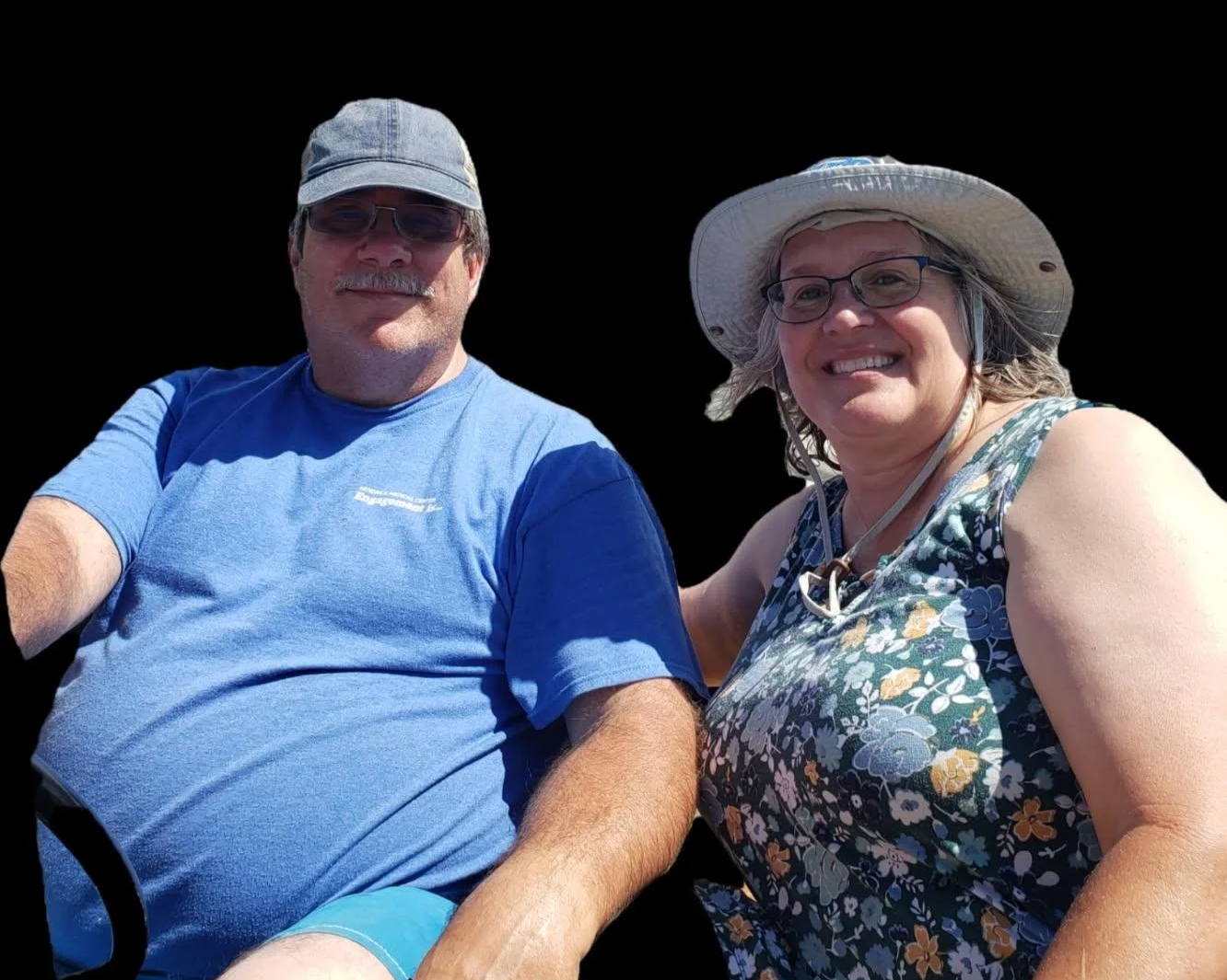 A smiling man and woman outdoors, both wearing hats and sunglasses. The woman is wearing a floral dress, and the man is in a blue t-shirt. The background is plain black.