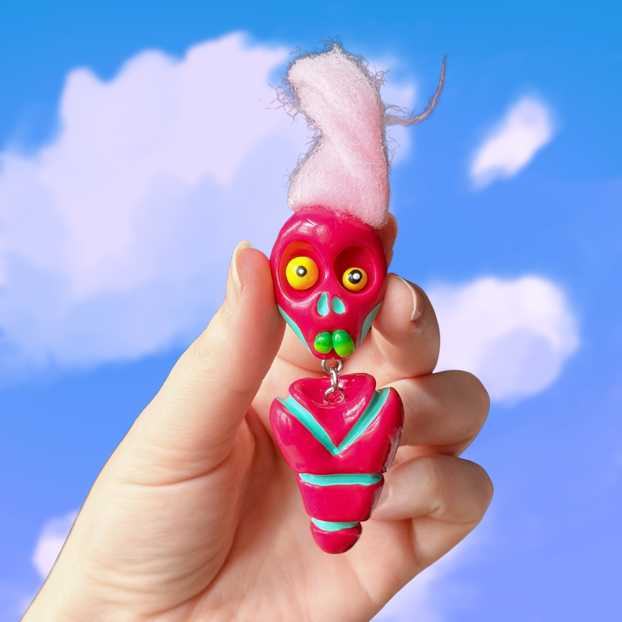 Polymer clay berry colored fidget that looks like a quirky skeleton with no arms or legs and pink hair. Photographed on top of a cloudy sky background.