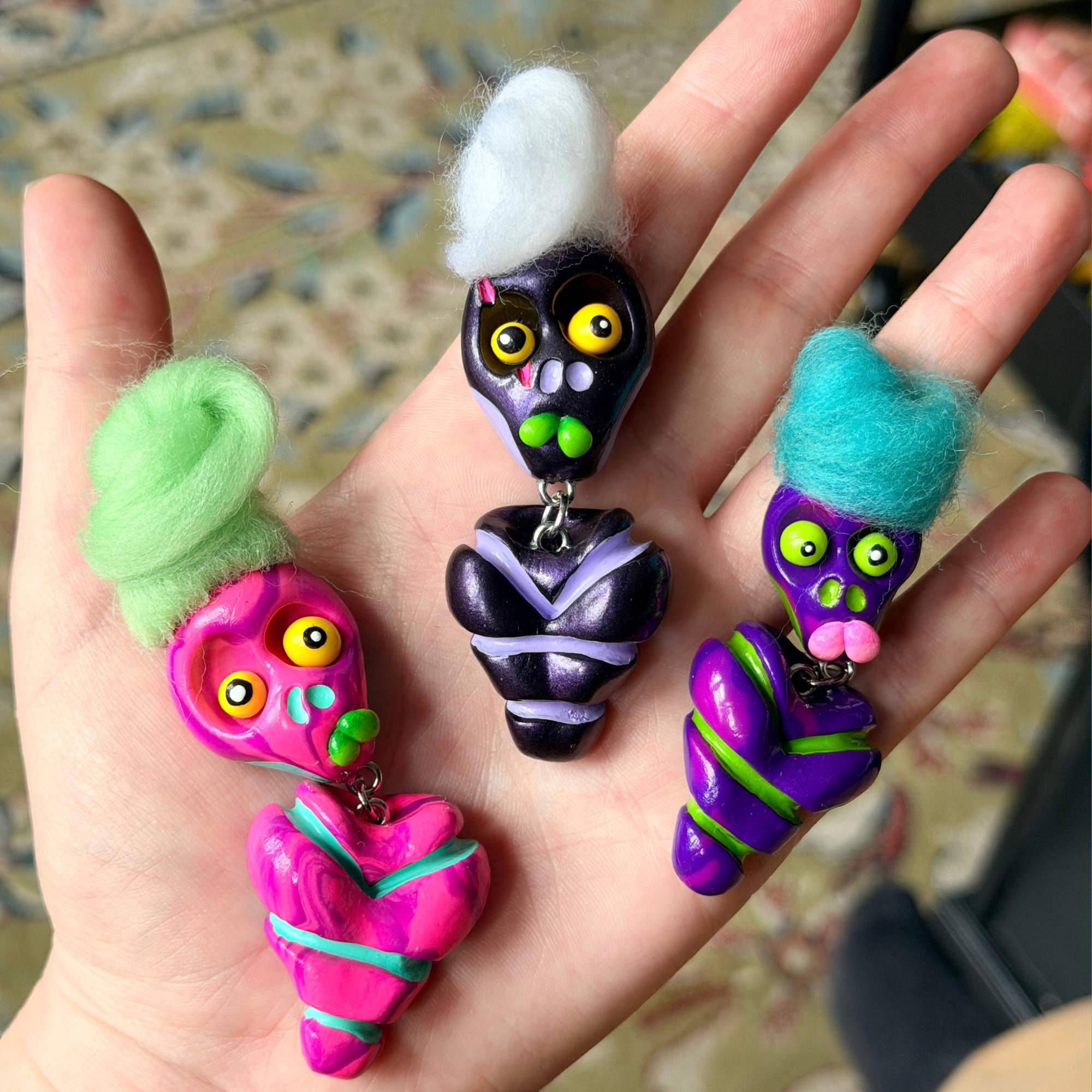Three bone daddy fidgets. One marbled pink, one spotted purple, one metallic purple photographed in hand.