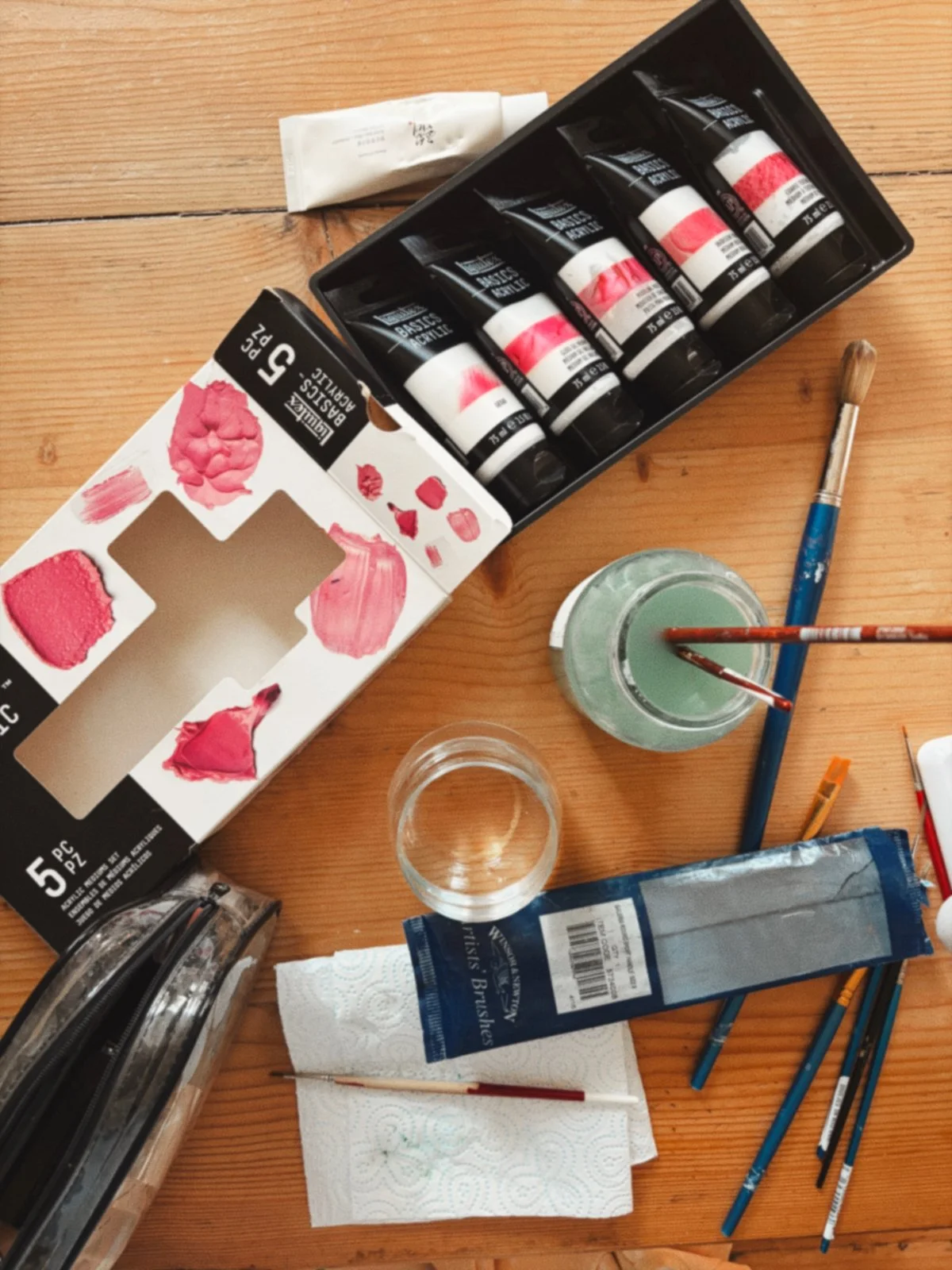 An overhead flatlay shot of acrylic mediums, paintbrushes in water, and art supplies