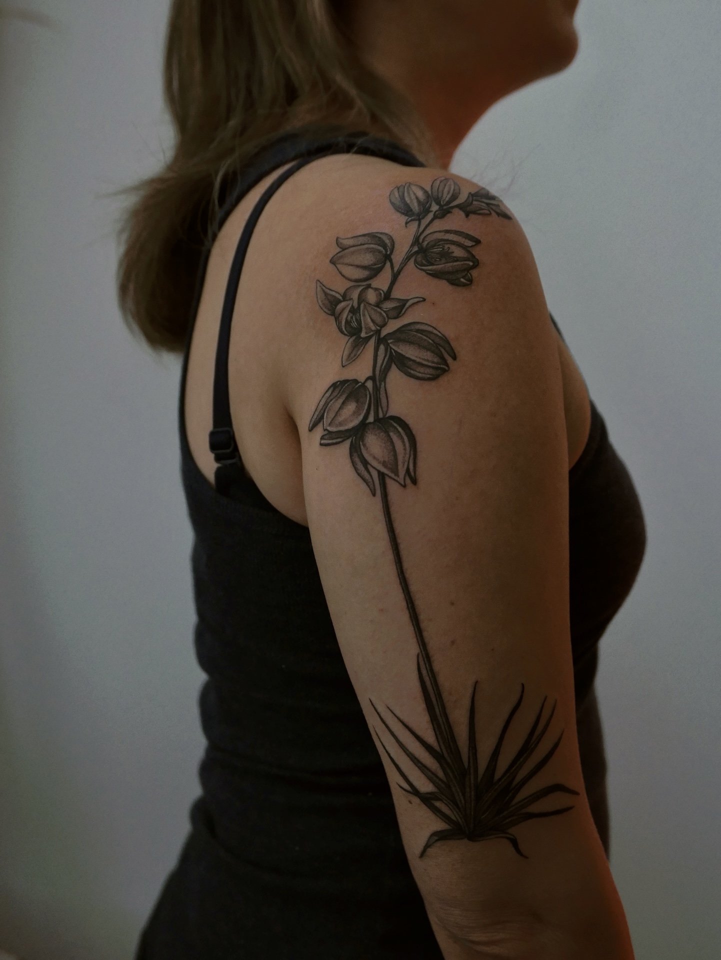 detailed blackwork botanical illustration tattoo of flowering yucca lowing upper arm