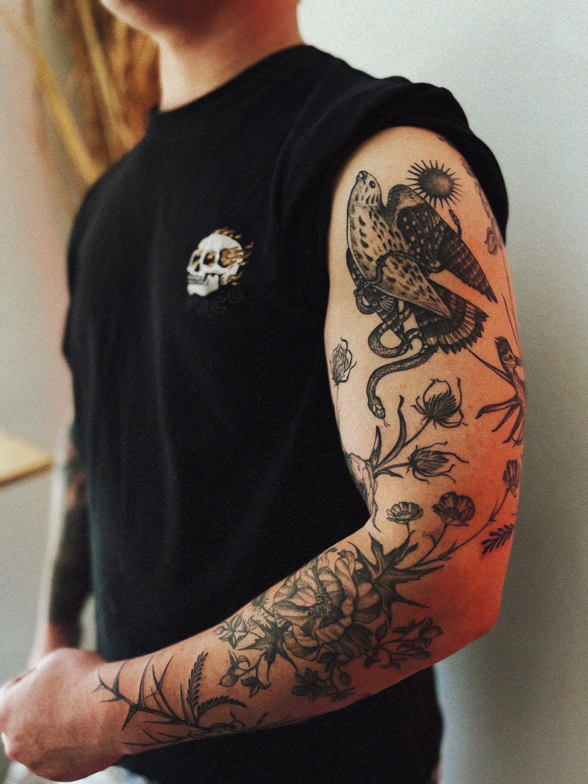 Southwest-inspired blackwork tattoo sleeve with a hawk, snake, sun, and wildflowers wrapping the arm