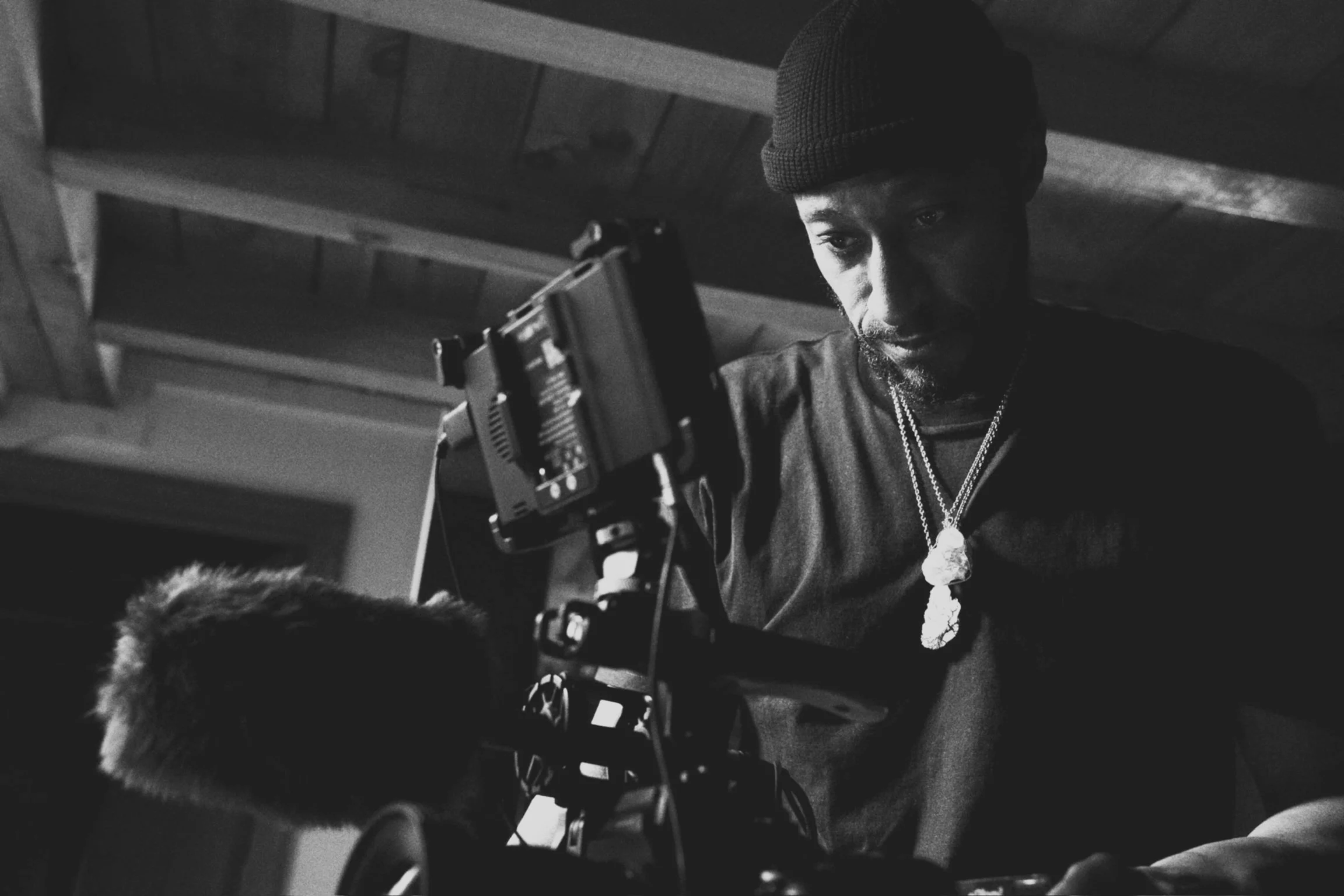Black and white photo of a man wearing a beanie, looking at an object, possibly a camera or equipment, with a focused expression