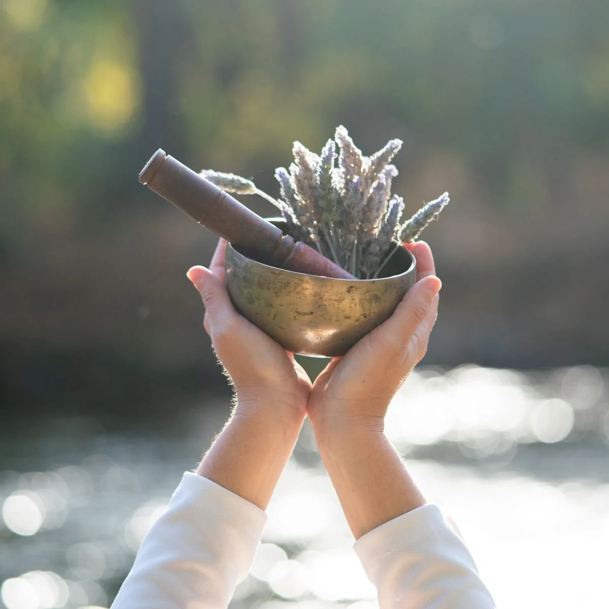 hands holding up a small singing bowl and sage over a river