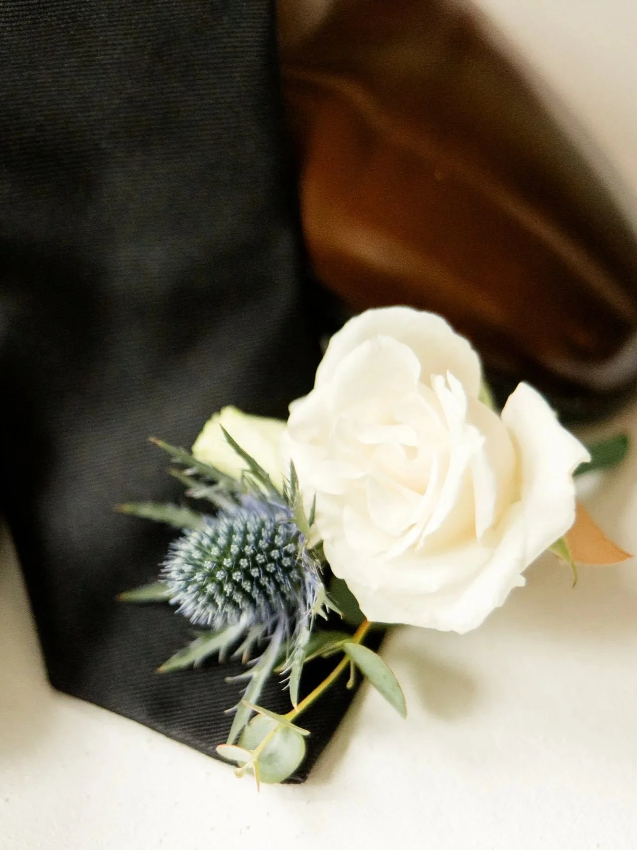 A white rose with a purple thistle and green foliage in a black wrapping