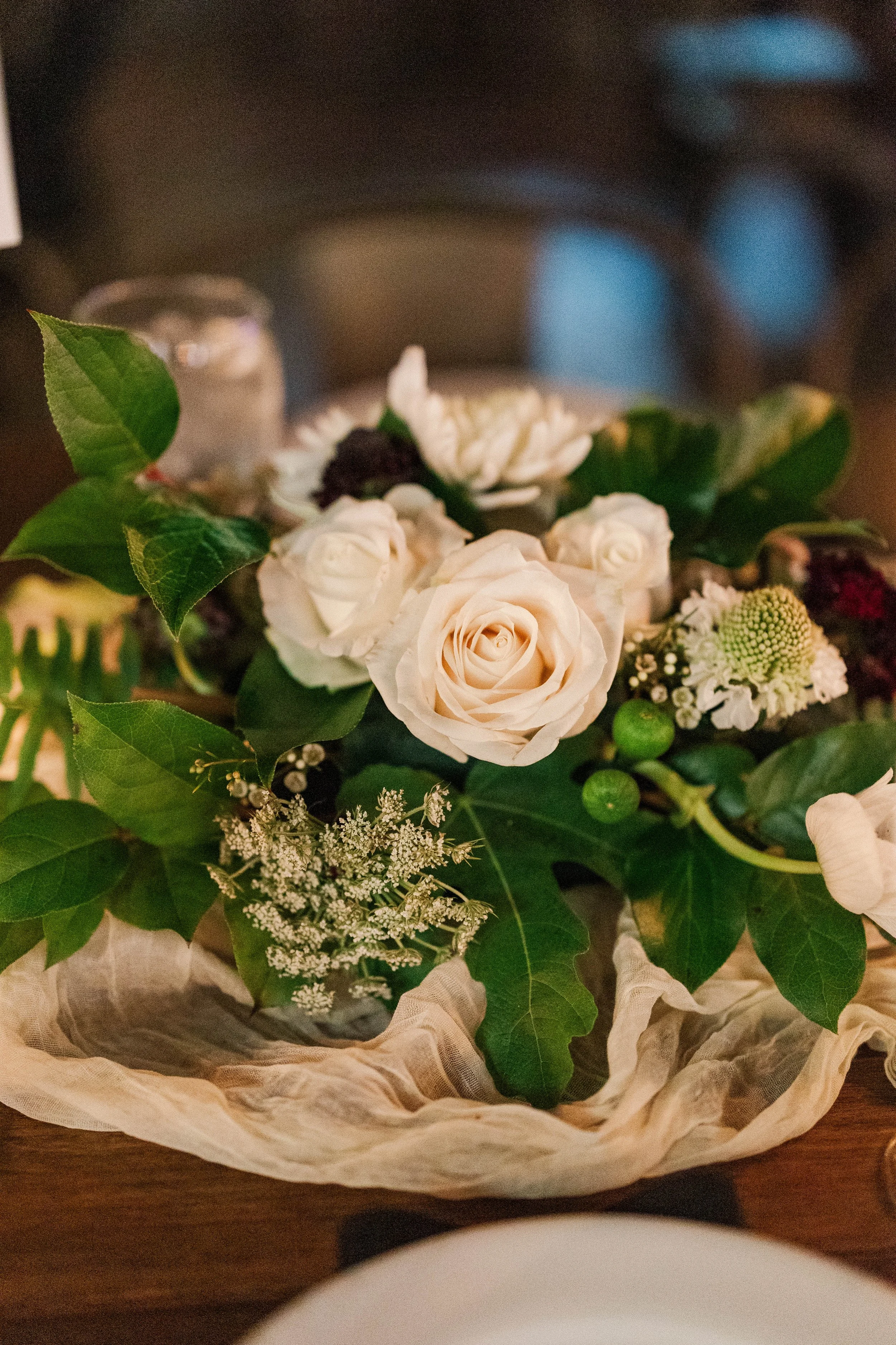 A bouquet of white roses, greenery, and baby's breath arranged on a table, wrapped in decorative paper.