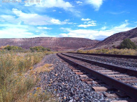 Railroad tracks running through a hilly landscape under a blue sky with clouds.