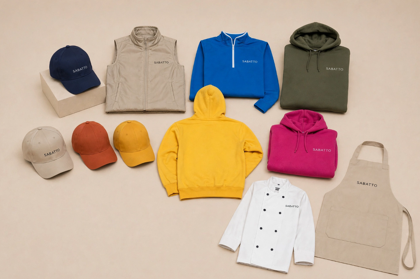 Varias prendas y accesorios de ropa de diferentes colores y estilos, incluyendo gorras, sudaderas, chaquetas, un chef, un delantal y un chaleco, todos con la marca 'SABATTO'.
