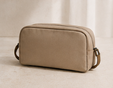 Neceser de color beige sobre una superficie, con fondo de cortina blanca.