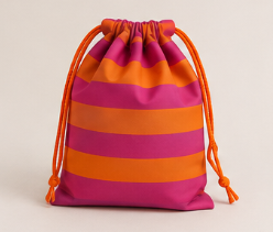 Un bolso de tela con rayas horizontales en colores rosa y naranja y cuerdas anaranjadas para cerrar.