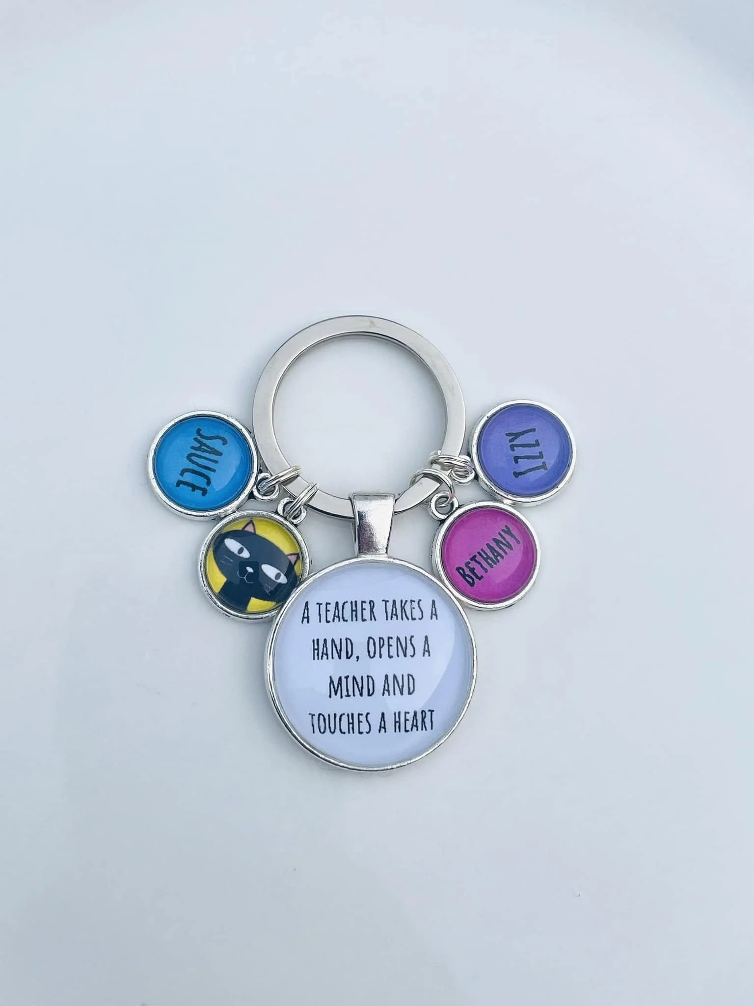A metal keychain with colorful charms, including a black cat, with a quote about teachers