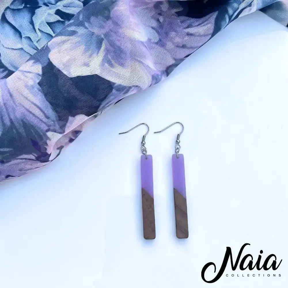 Purple and brown rectangular dangle earrings resting on a white surface with purple floral fabric nearby.