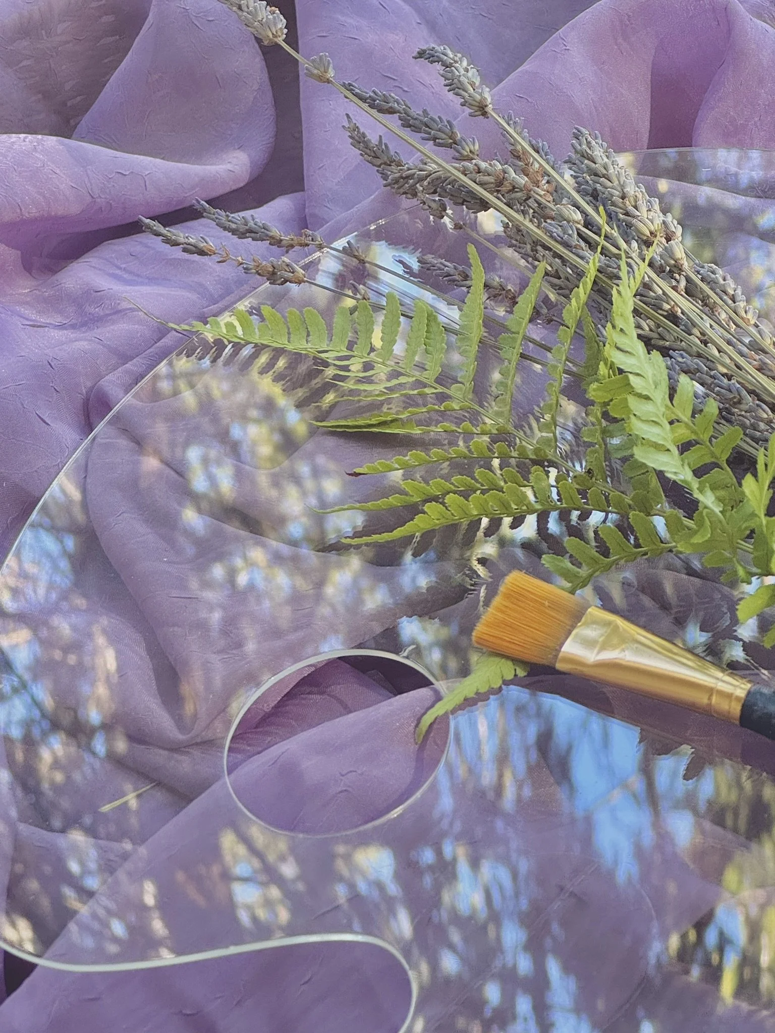 A lavender bouquet wrapped in purple paper, placed on purple fabric, with a small yellow-brown paintbrush nearby.