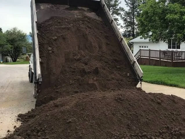 Dump truck unloading a large pile of dirt onto the driveway.