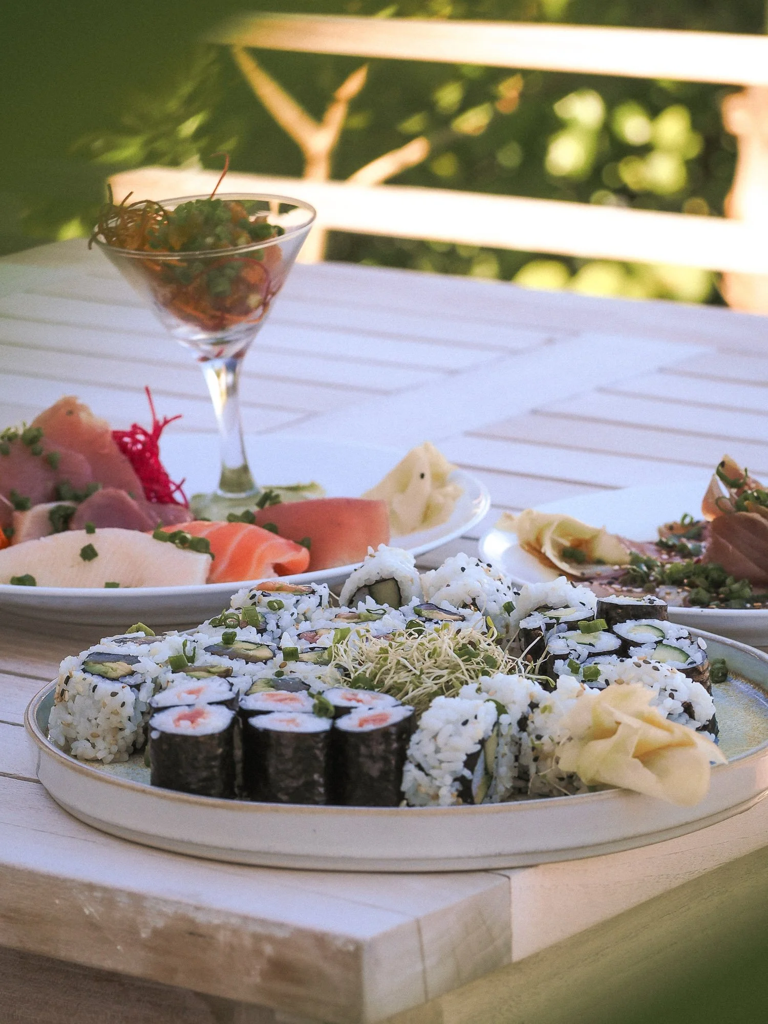 Close-up of a sushi platter with various types of sushi rolls on a white plate, placed on a wooden table.