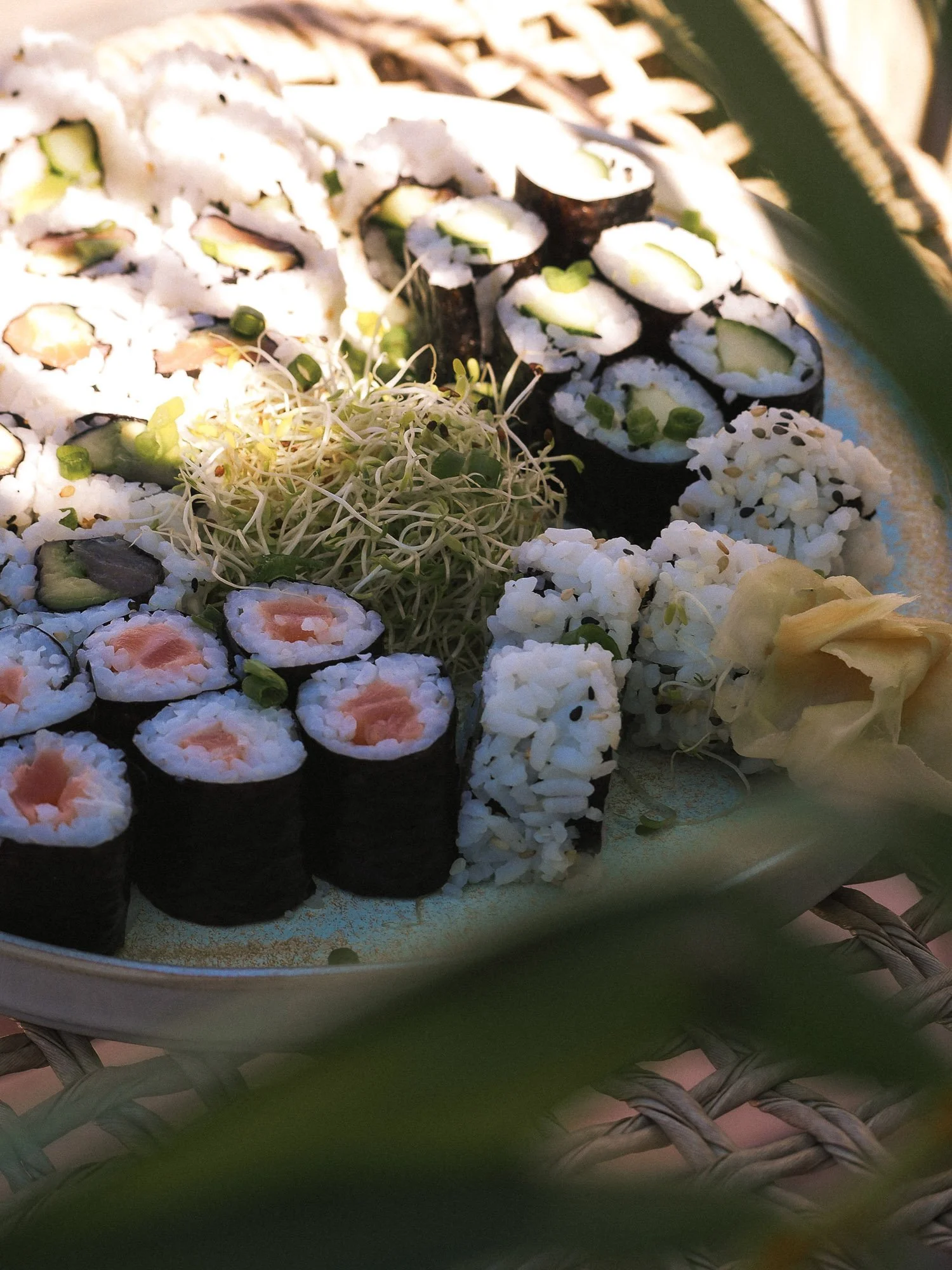 Assorted sushi rolls with rice, cucumber, salmon, and possibly tuna, garnished with sprouts, served on a plate.