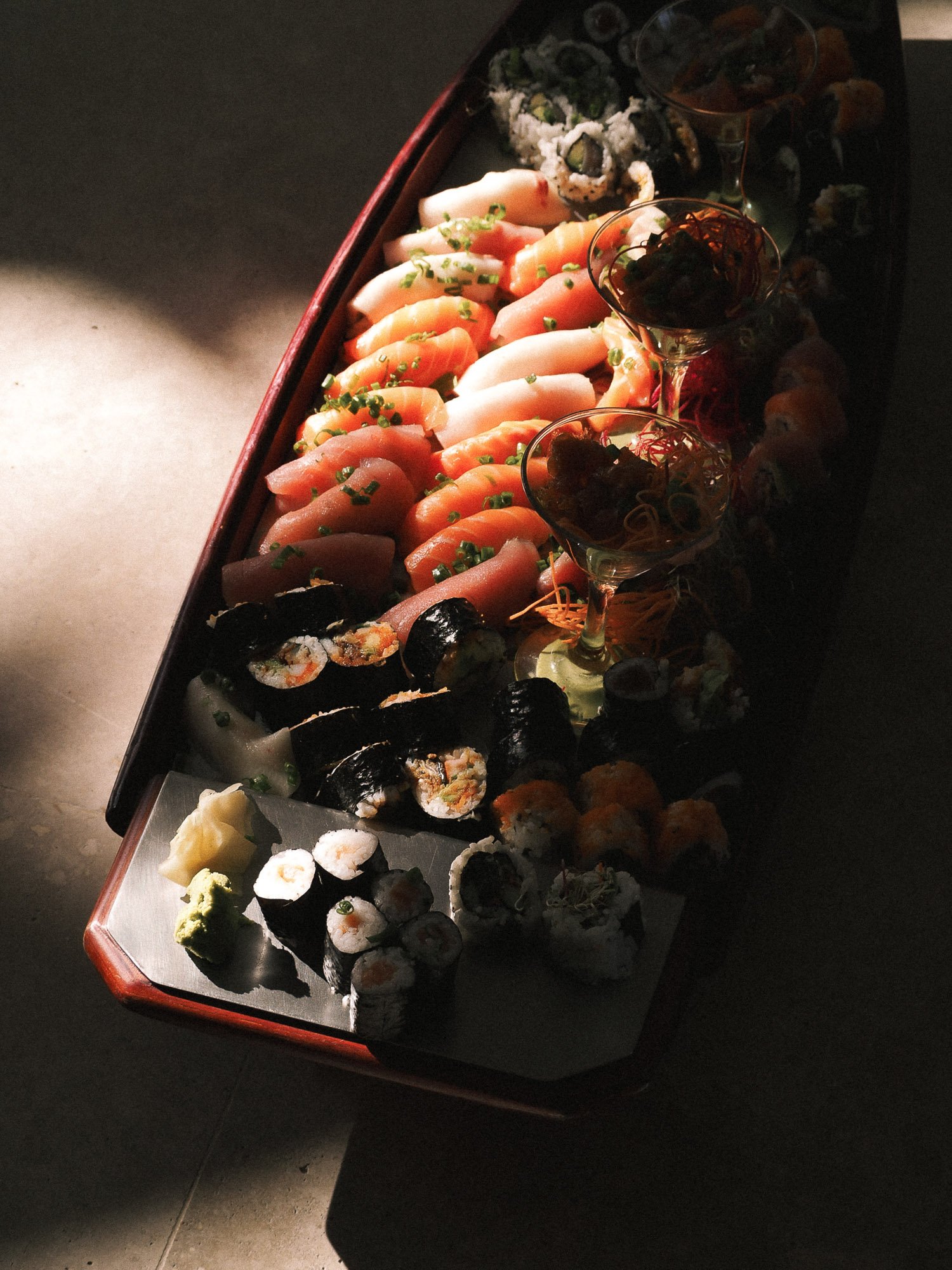 Assorted sushi rolls and sashimi on a tray, decorated with wasabi and garnishes, in a dimly lit setting.