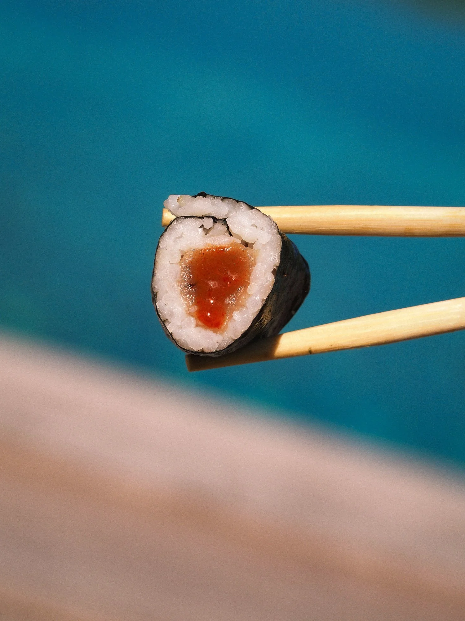A piece of sushi held by chopsticks with a blue background.
