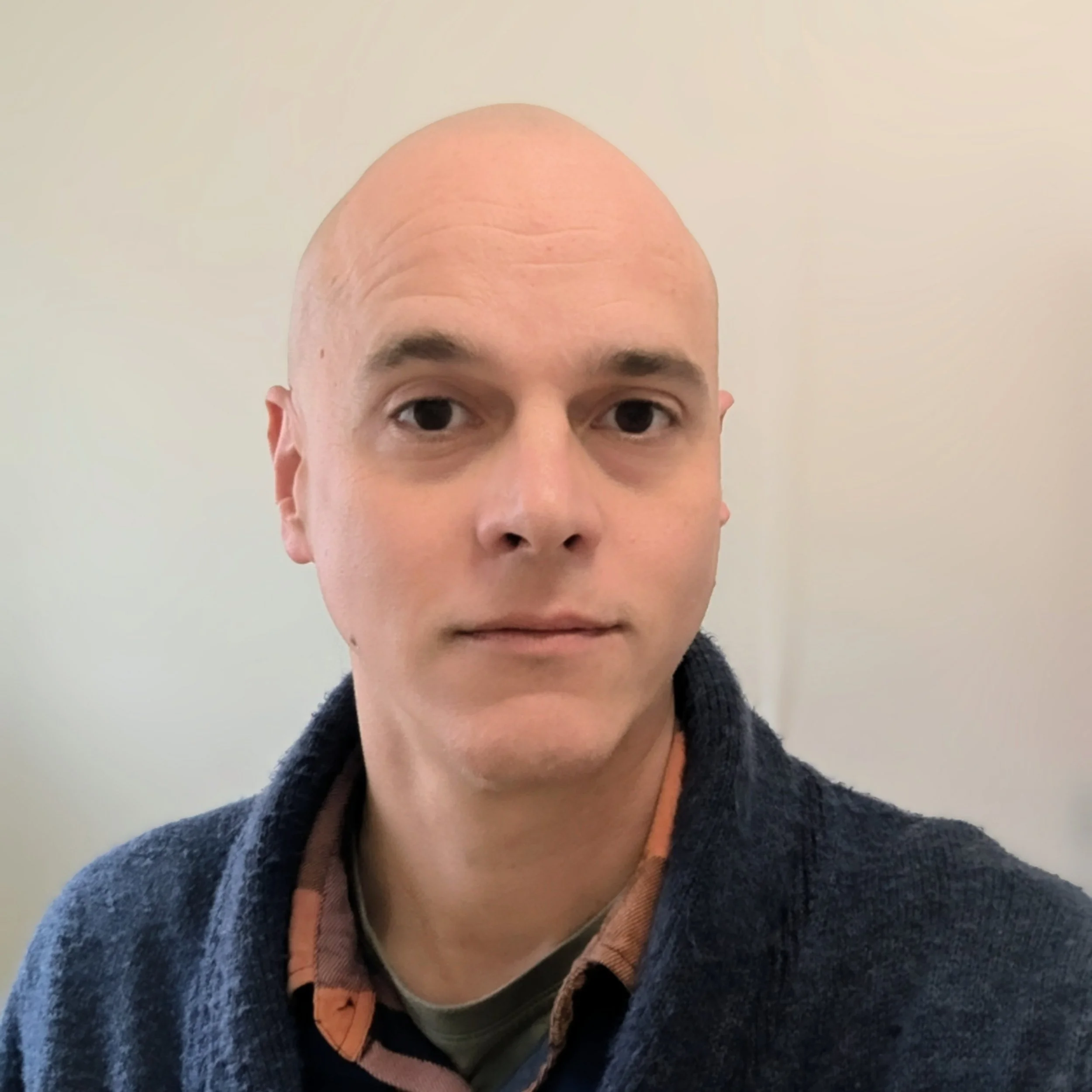 Close-up of a person's face showing mostly their forehead, eyes, and part of a hoodie. The person is bald with a neutral expression, set against a plain, light background.