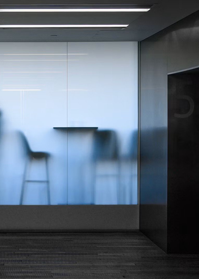 Blurred silhouette of chairs and a table seen through a glass wall in a modern office or conference room.