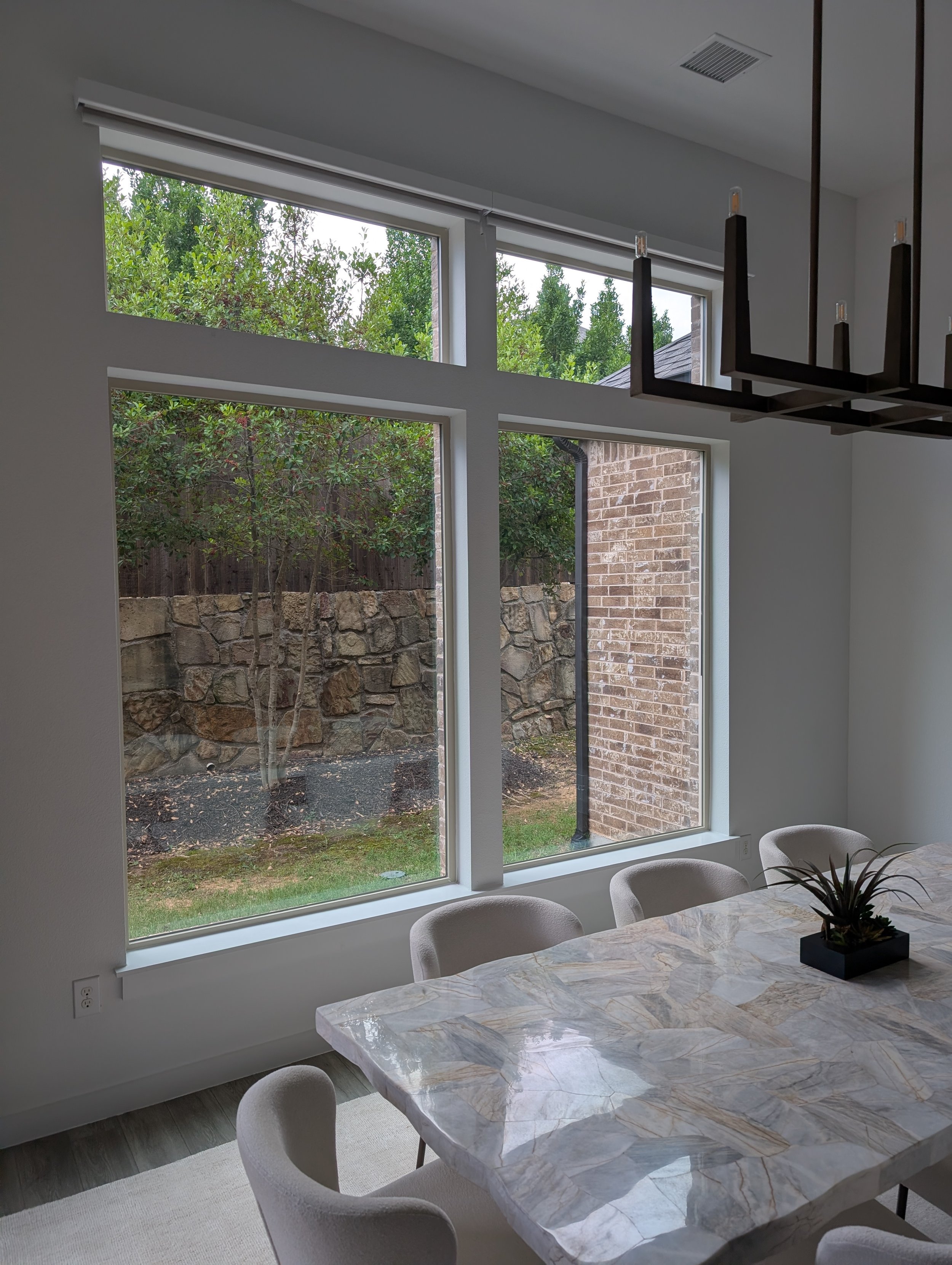 Dining room with large bay windows, marble table, white chairs, and a black pendant light fixture.