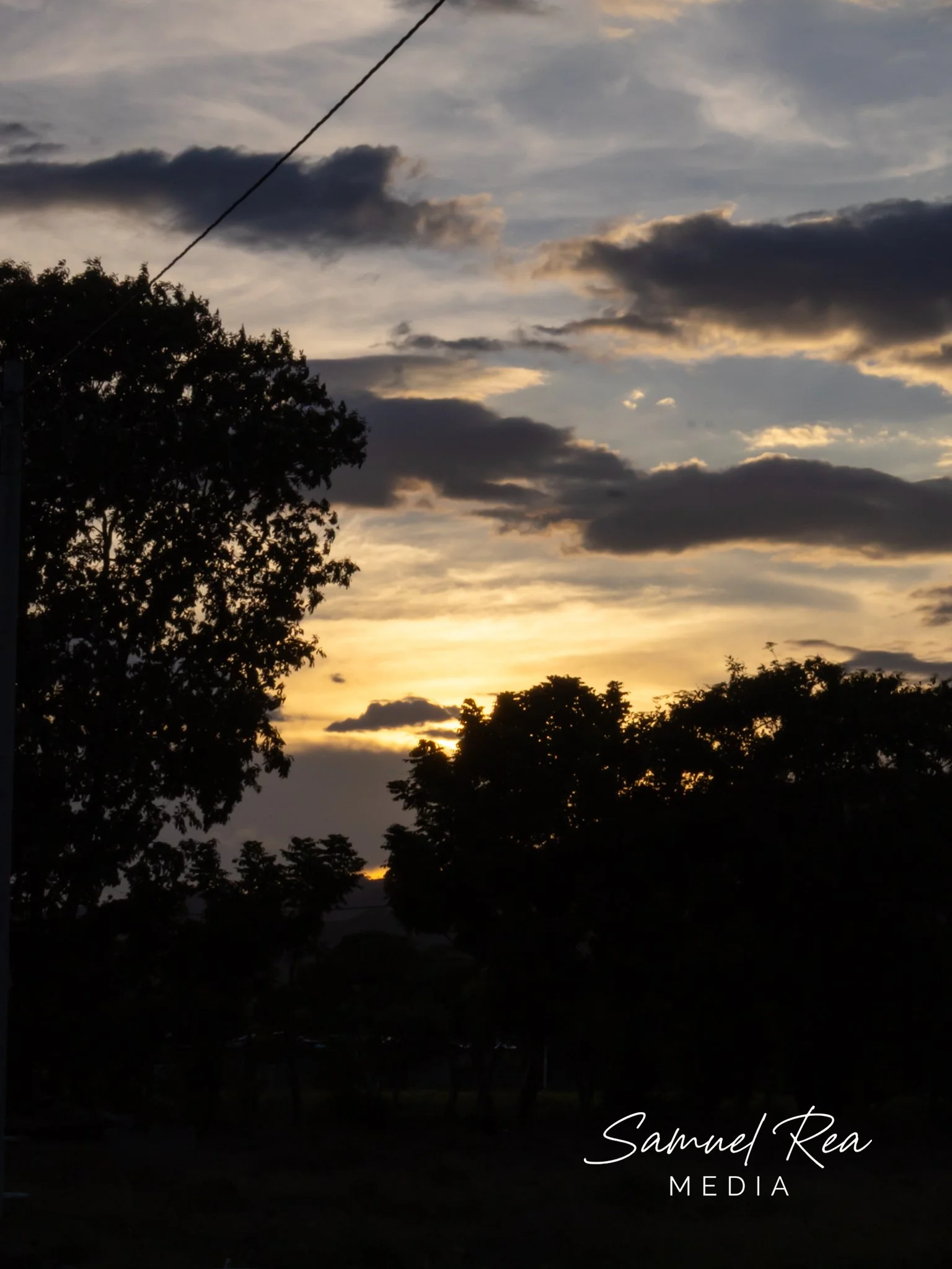 Sunset sky with dark clouds and silhouettes of trees in the foreground.