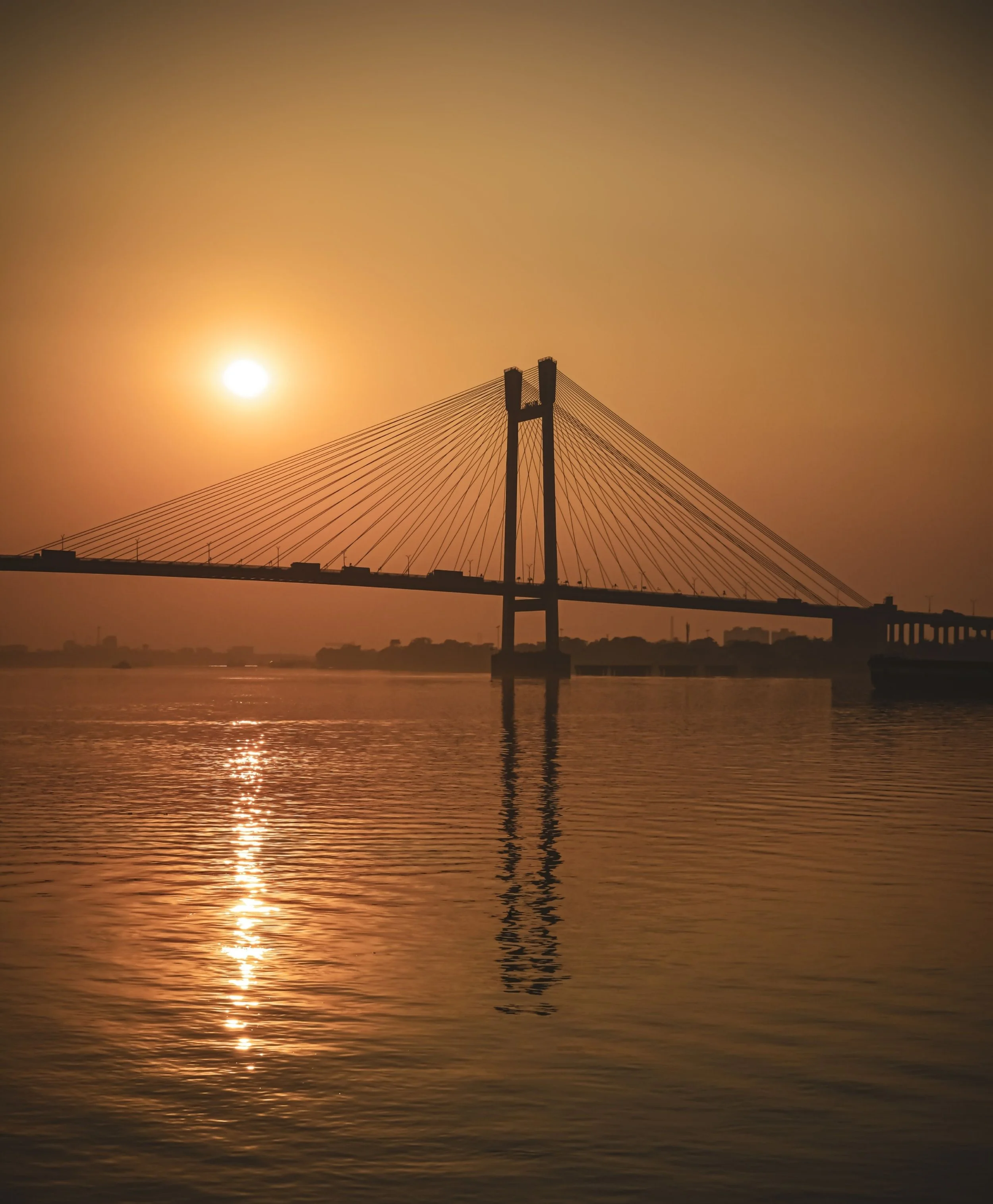 Bridge silhouetted against a sunset over calm water.