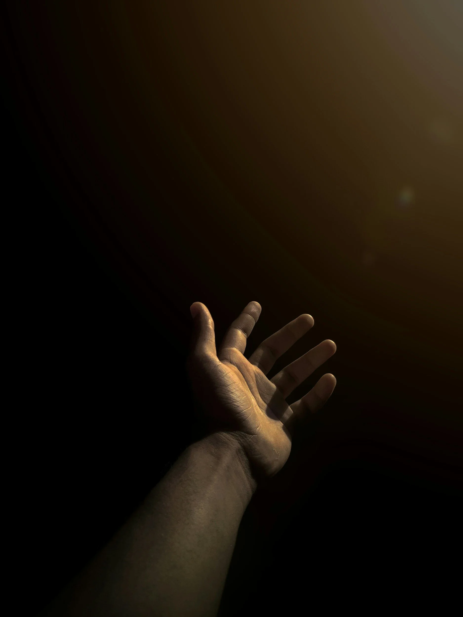 A hand reaching out towards a dark background, with some light illuminating the fingers.
