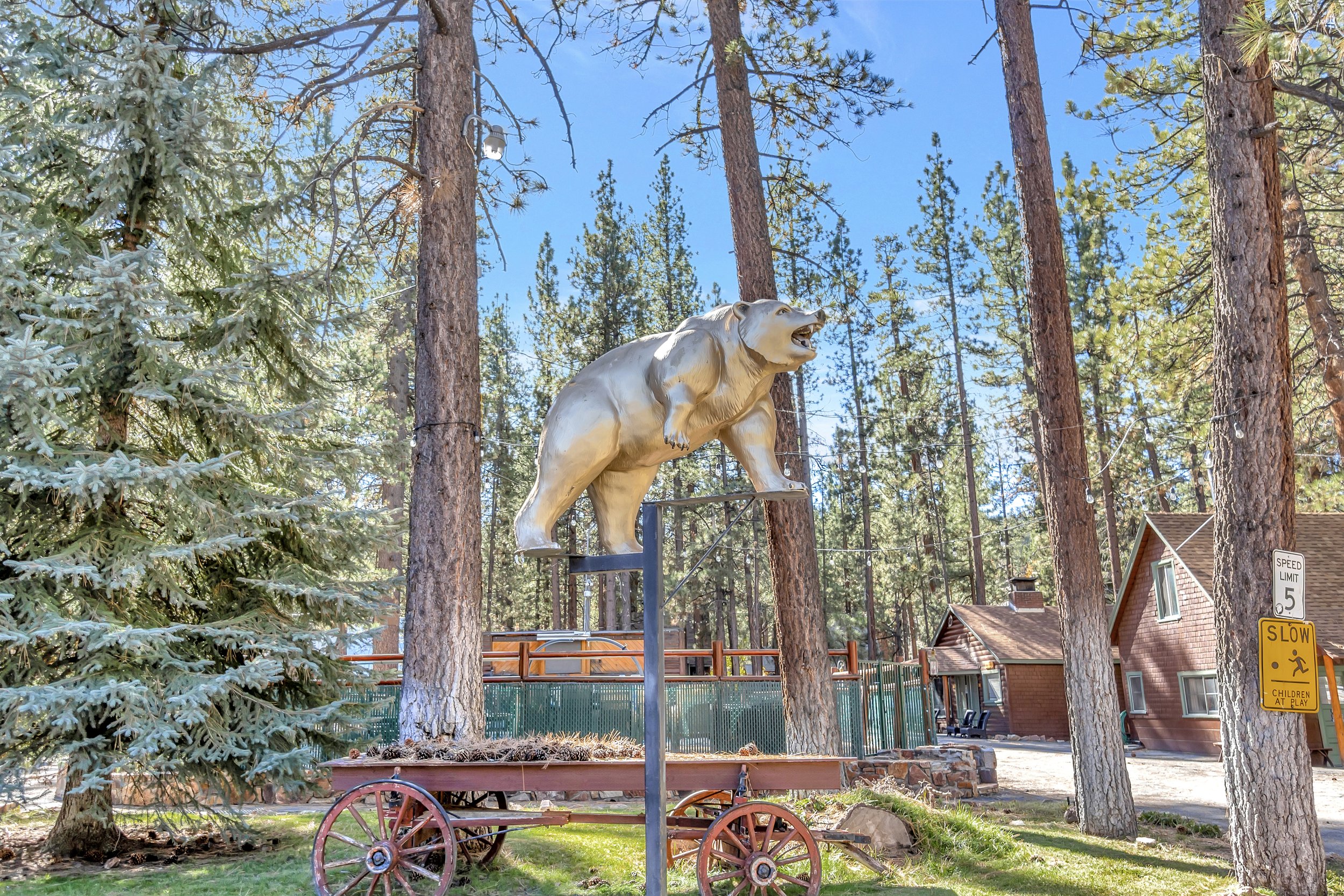 A large statue of a bear standing on a platform in a forested area with tall pine trees and a blue sky in the background.