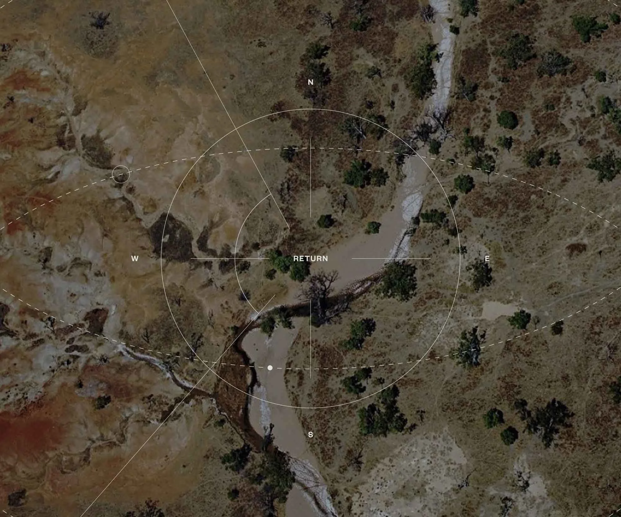 Aerial view of a dry, rocky landscape with patches of trees and a winding river running through it. The image includes overlays with cardinal directions and a dashed white line indicating a route.